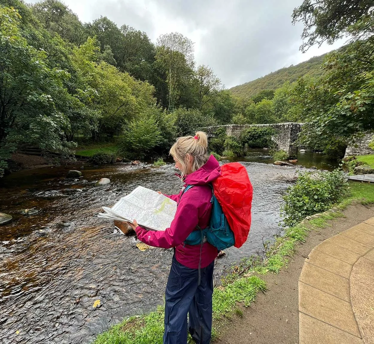 Woman reading a map next to a flowing river, wearing waterproof jacket and trousers