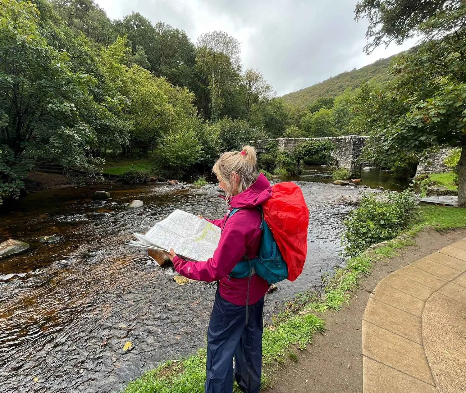 Woman reading a map next to a flowing river, wearing waterproof jacket and trousers