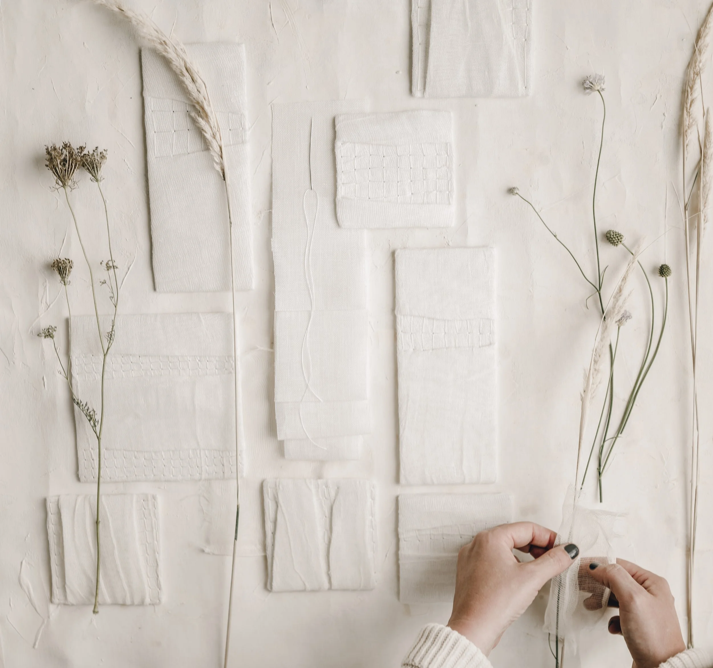 Beautifully styled textile wall art pieces with plants layed out on a white backgound.