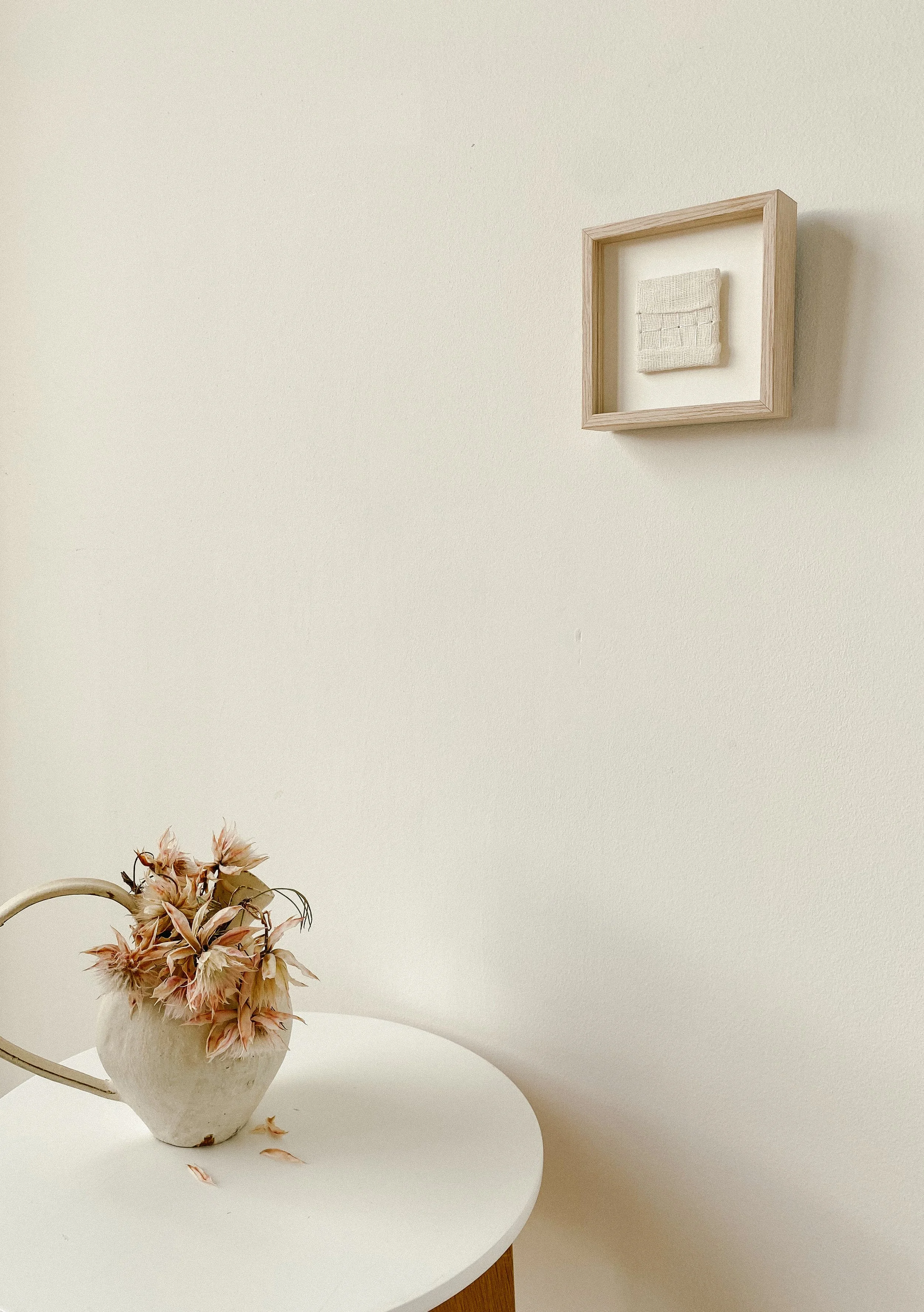Textile wall art is hanging on the wall framed in a wooden oak frame, dimensions are 10 by 10 centimeters.