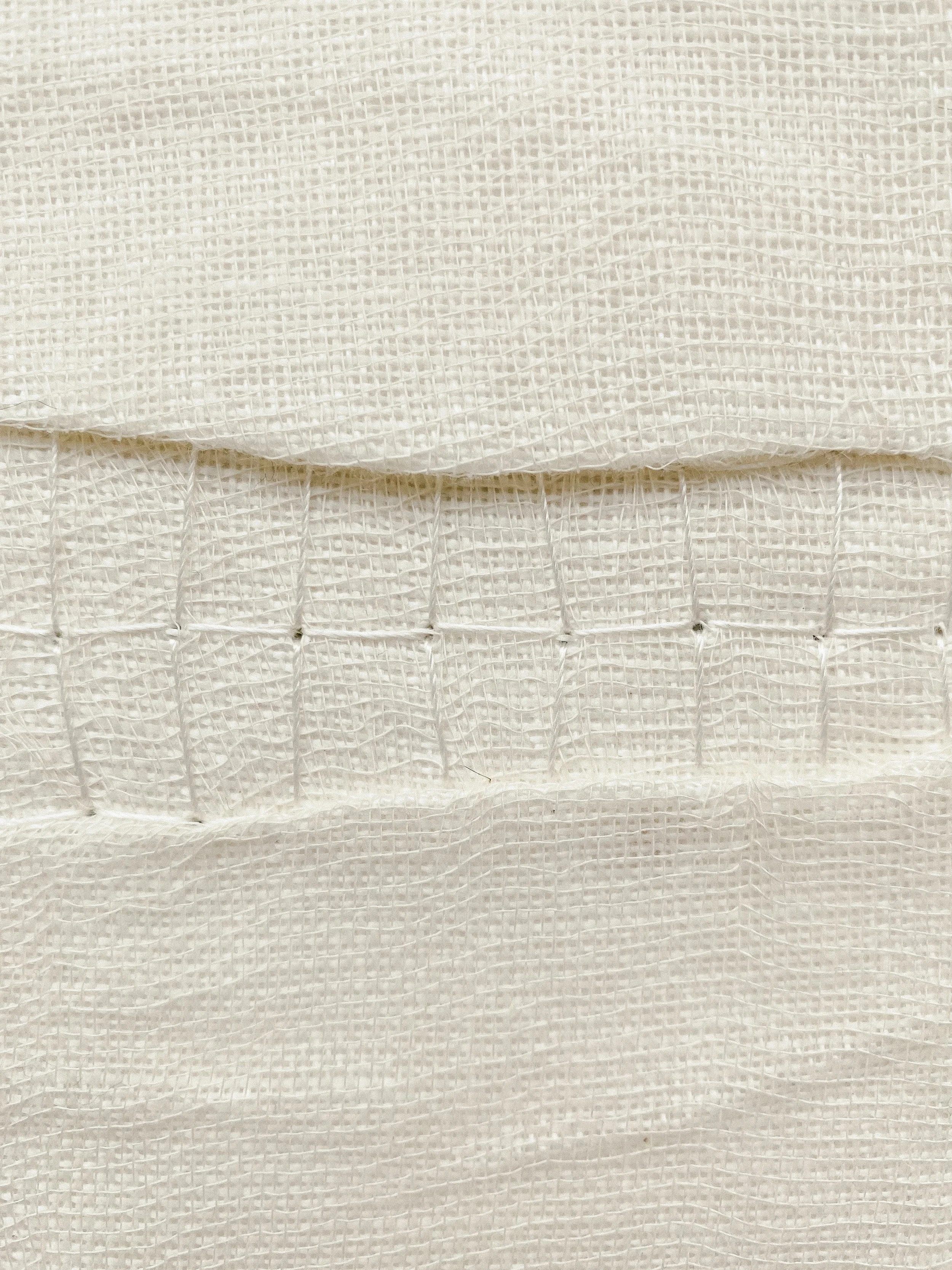 Zoomed-in image of textile wall art showing layers of fabric and sewn elements.