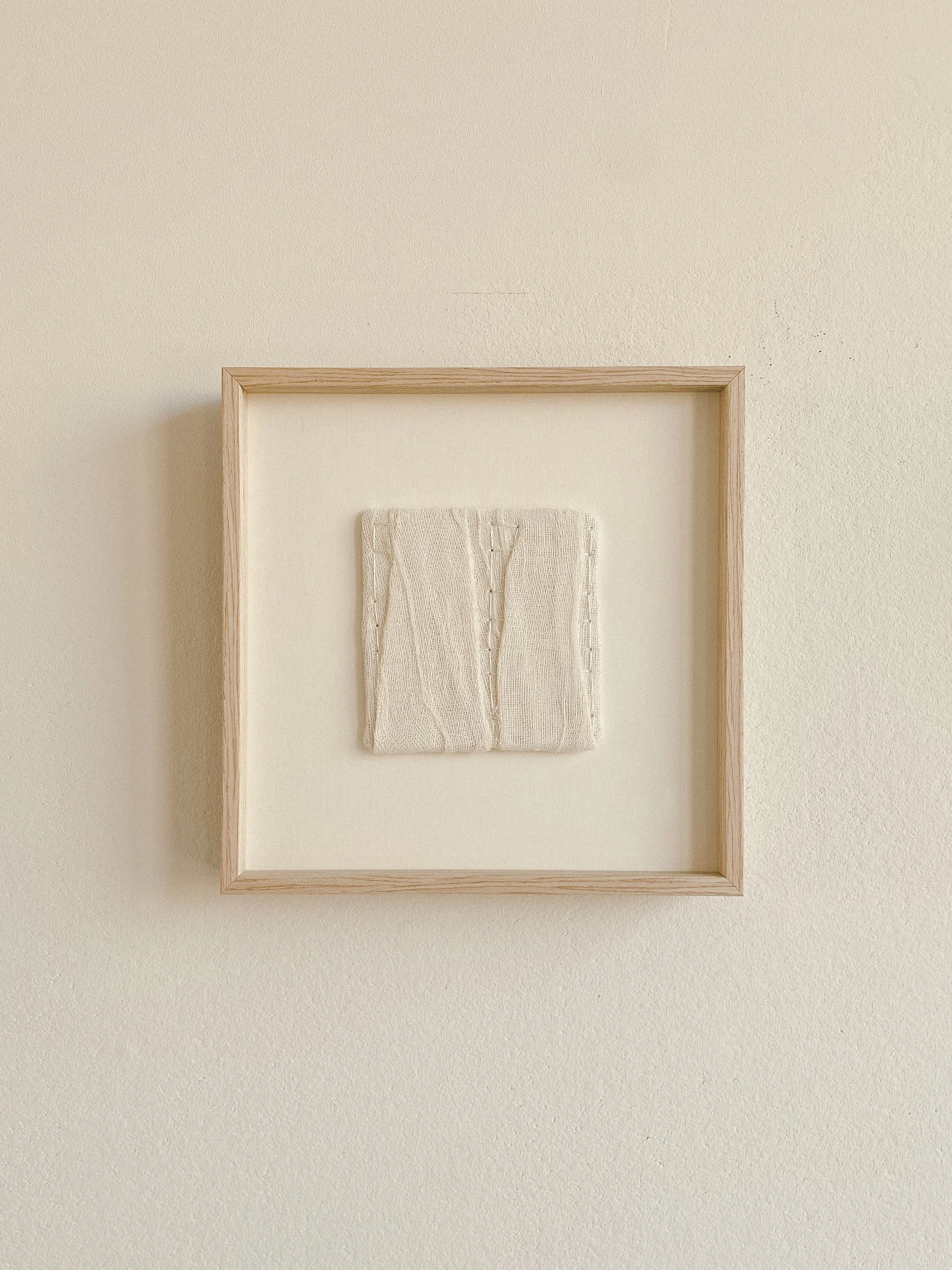 Textile wall art is hanging on the wall framed in a wooden oak frame, dimensions are 10 by 10 centimeters.