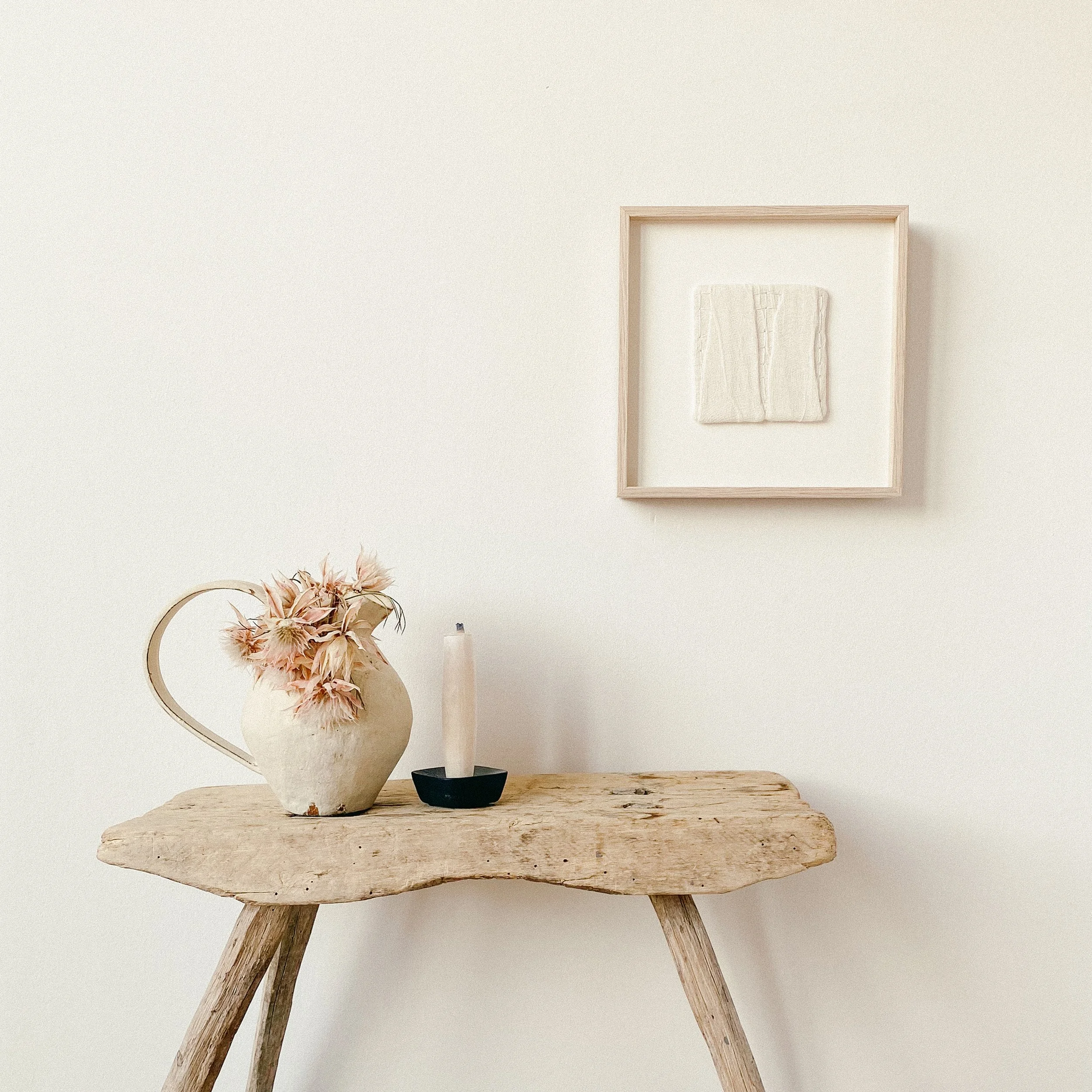 Textile wall art is hanging on the wall framed in a wooden oak frame, dimensions are 10 by 10 centimeters.