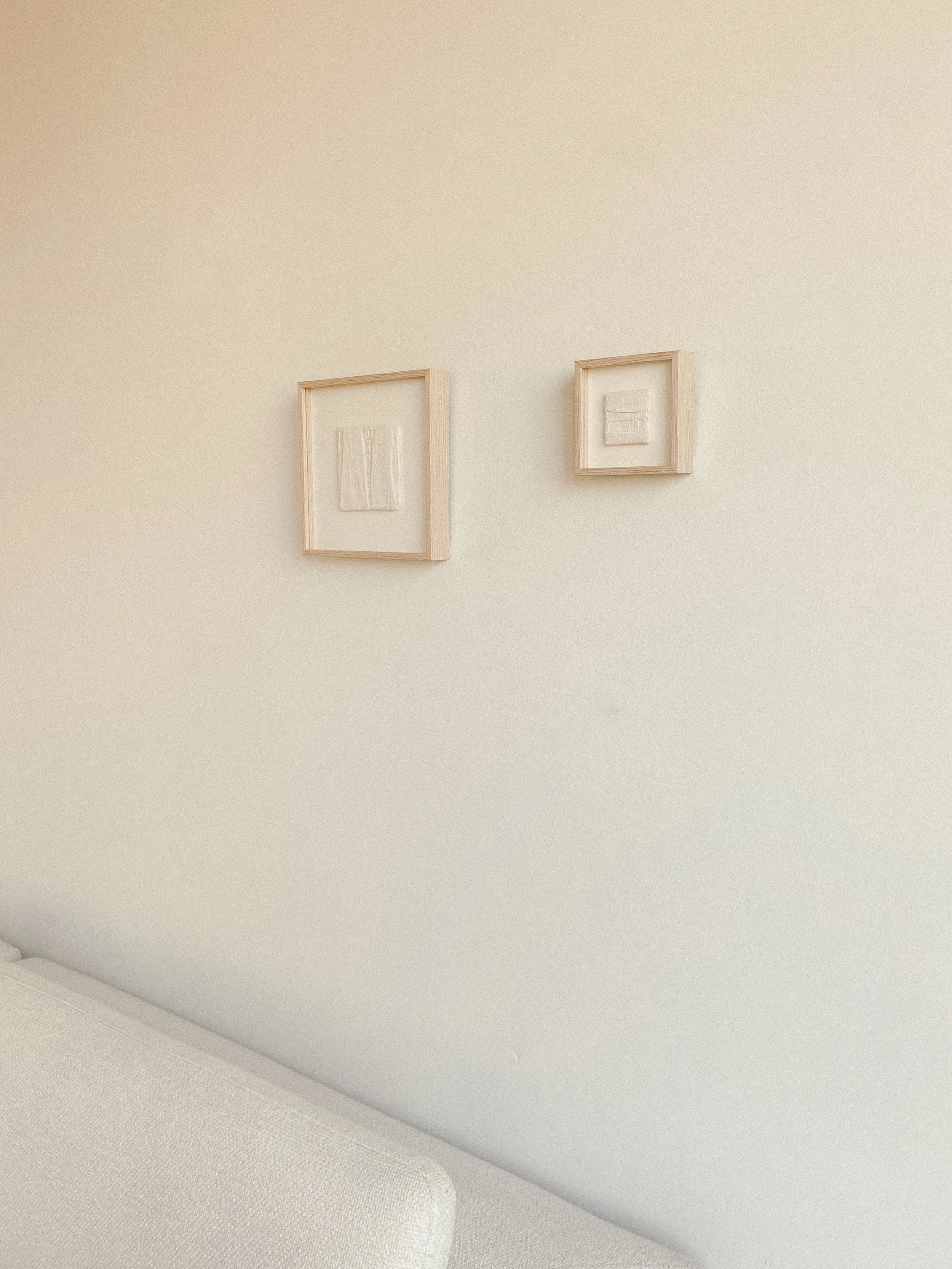 Two textile wall art pieces are hanging together  on the wall above a Bolia couch.
