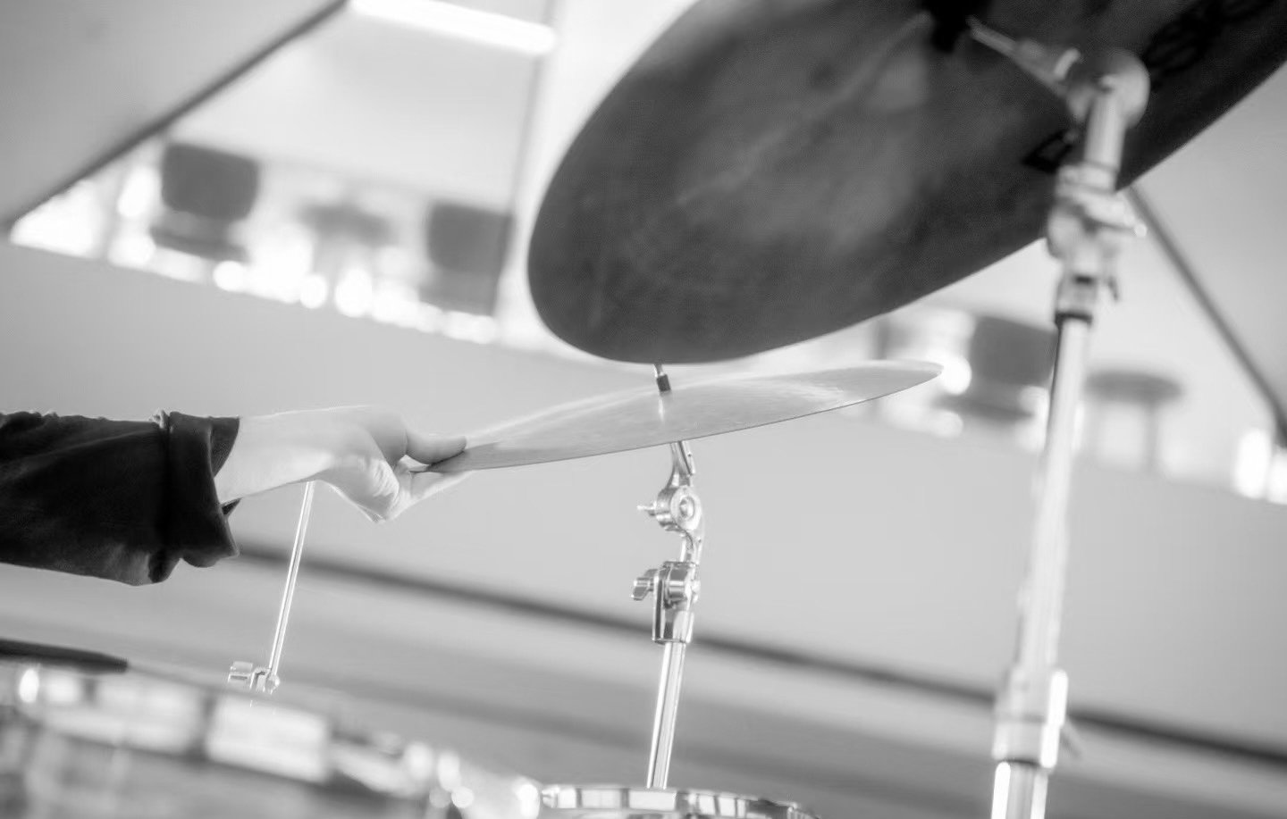 A person playing drums, holding a drumstick in front of a cymbal, in a black and white photo.