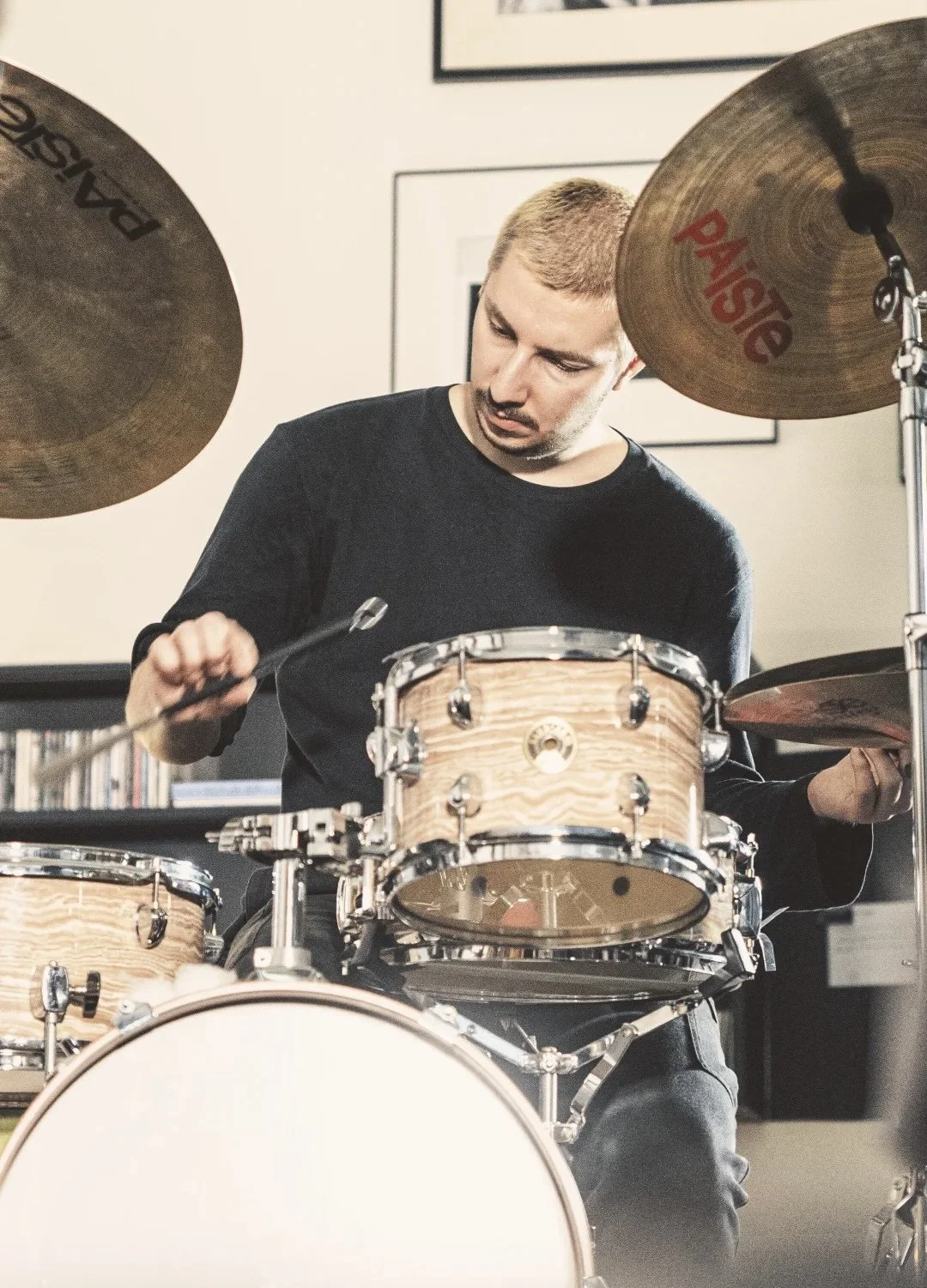 A man playing a drum set with wood finish drums and cymbals in a room.
