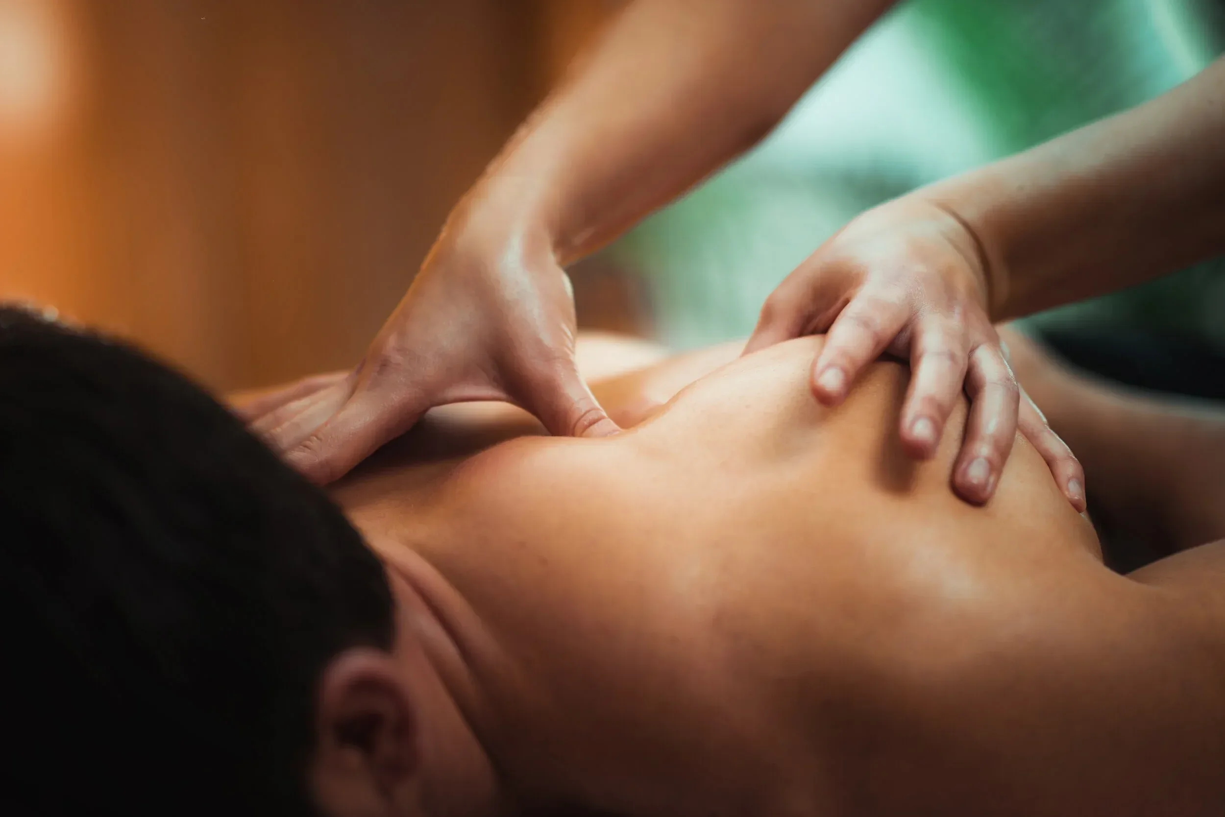 Close-up of a person receiving a massage, showing their back and shoulders as the massage therapist's hands apply pressure.