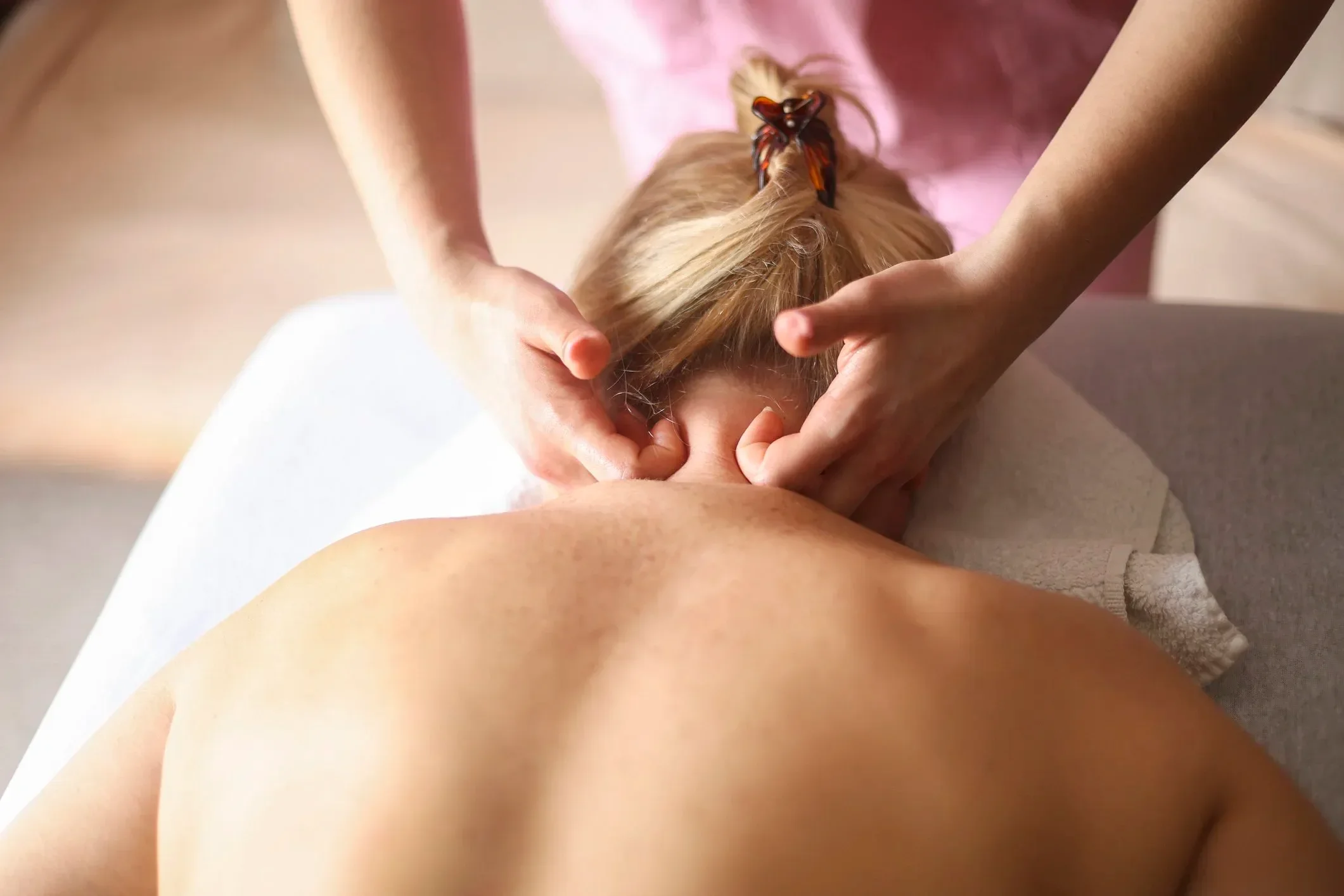 Person receiving a sports massage with hands on their back, revealing part of their shoulder and neck, in a peaceful setting.