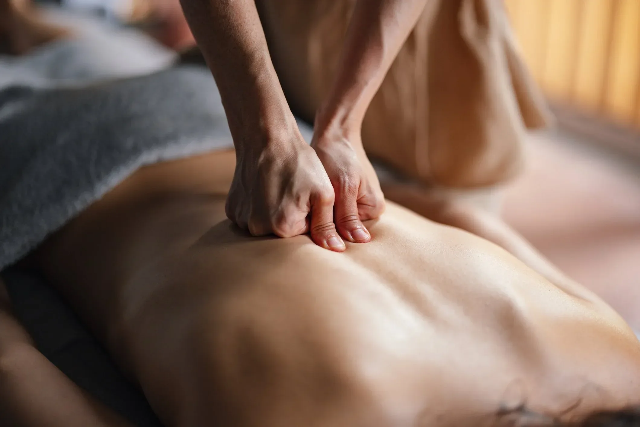 Close-up of a massage therapist giving a deep tissue massage with their hands on a client's back.