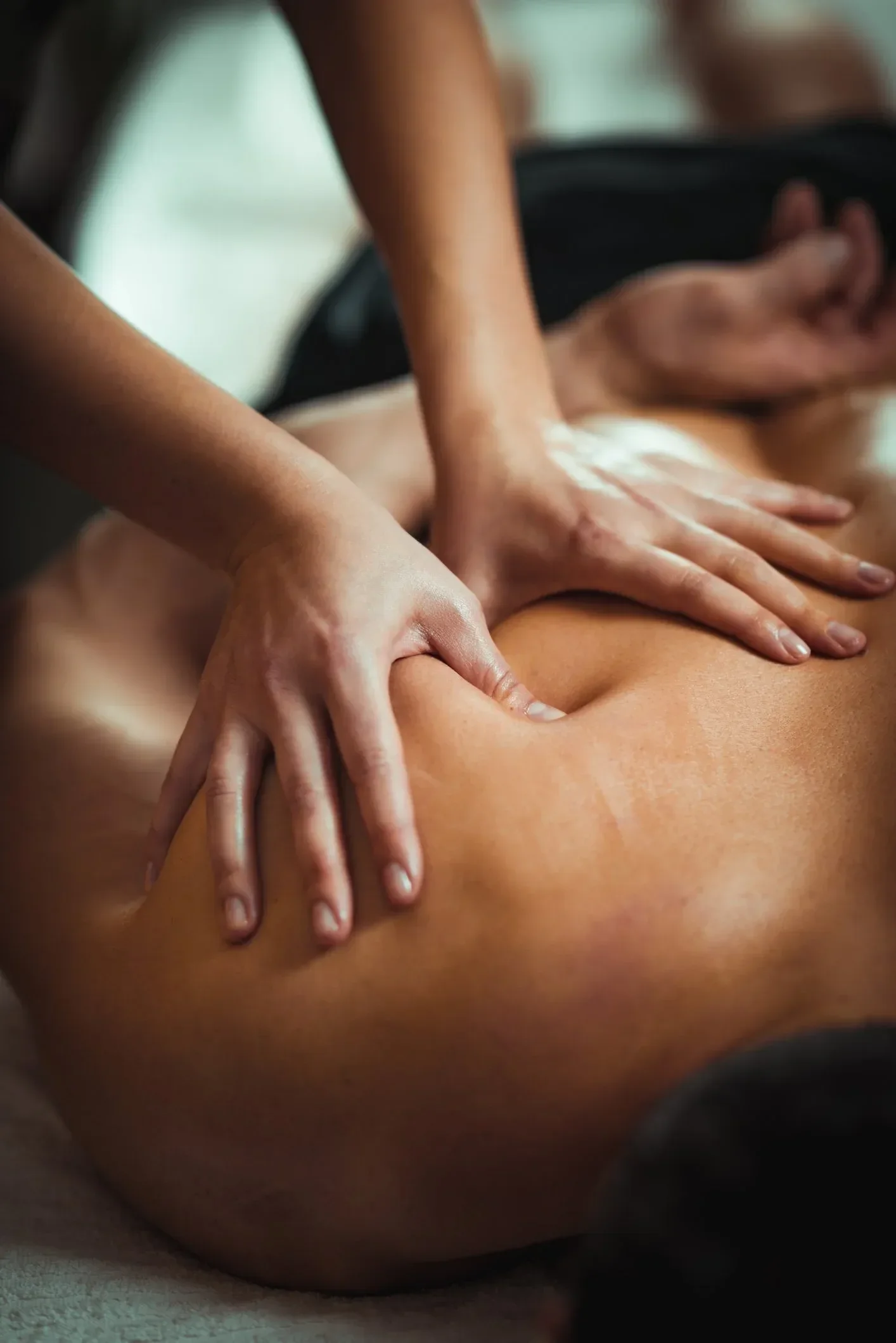 A person receiving a deep tissue massage, with hands on their back, in a peaceful setting.