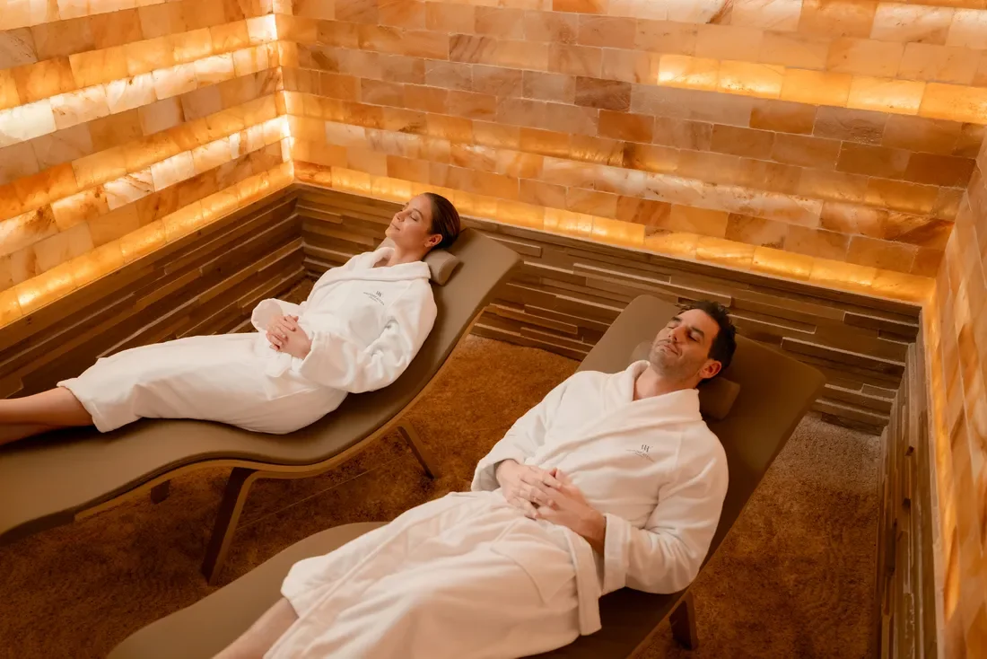 Two people relaxing on lounge chairs in salt therapy room with orange salt brick walls.