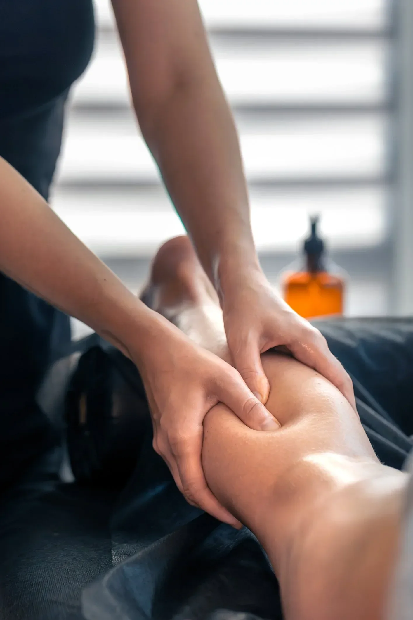 A person receiving a massage on their arm in a well-lit room with a bottle in the background.