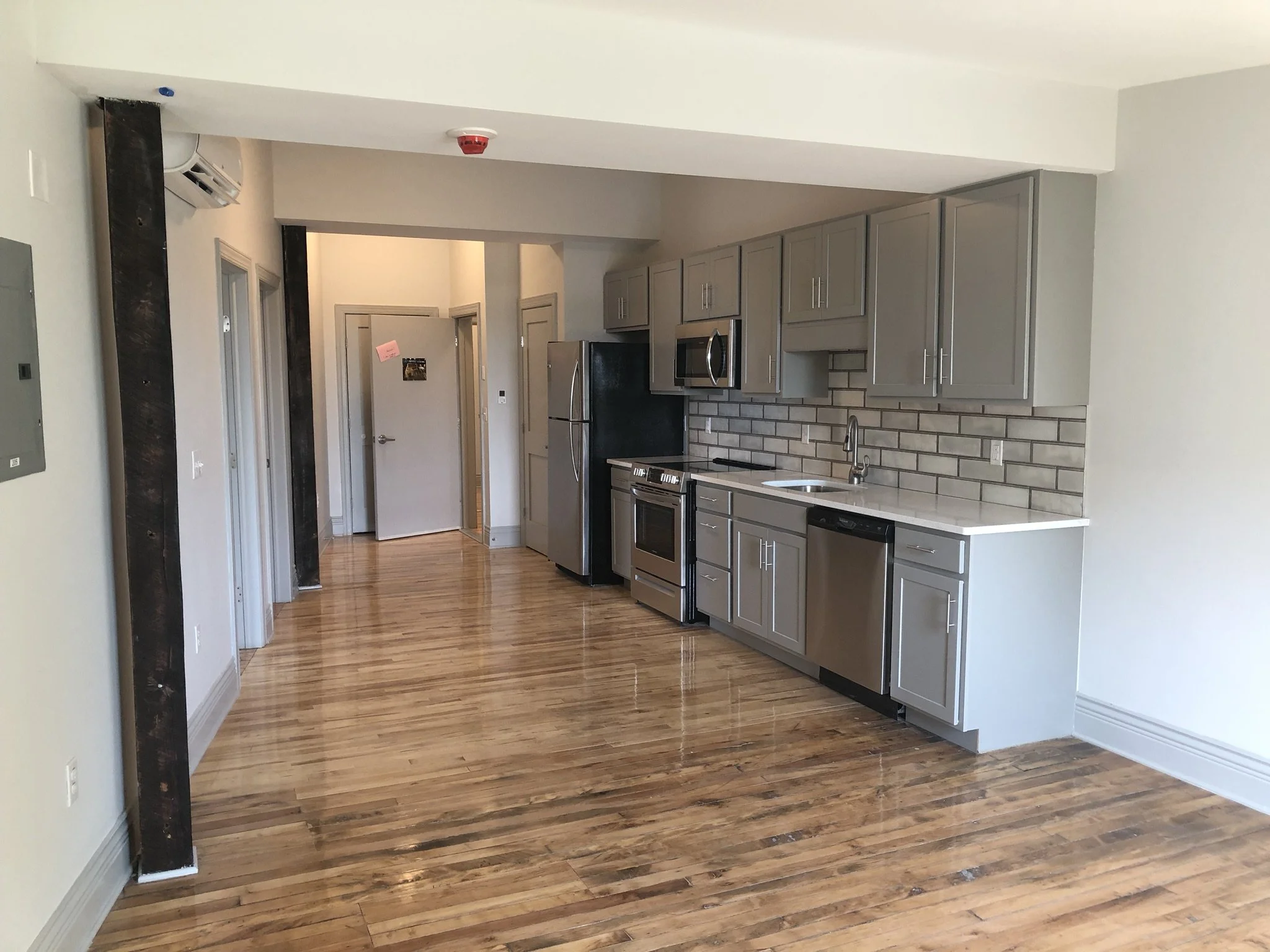 This kitchen shows how a small space can do a lot! The cool toned tile backsplash paired with the gray of the wooden cupboards creates a clean and earthy feel, flowing into the natural wood flooring and support beams. Including all of the essential a
