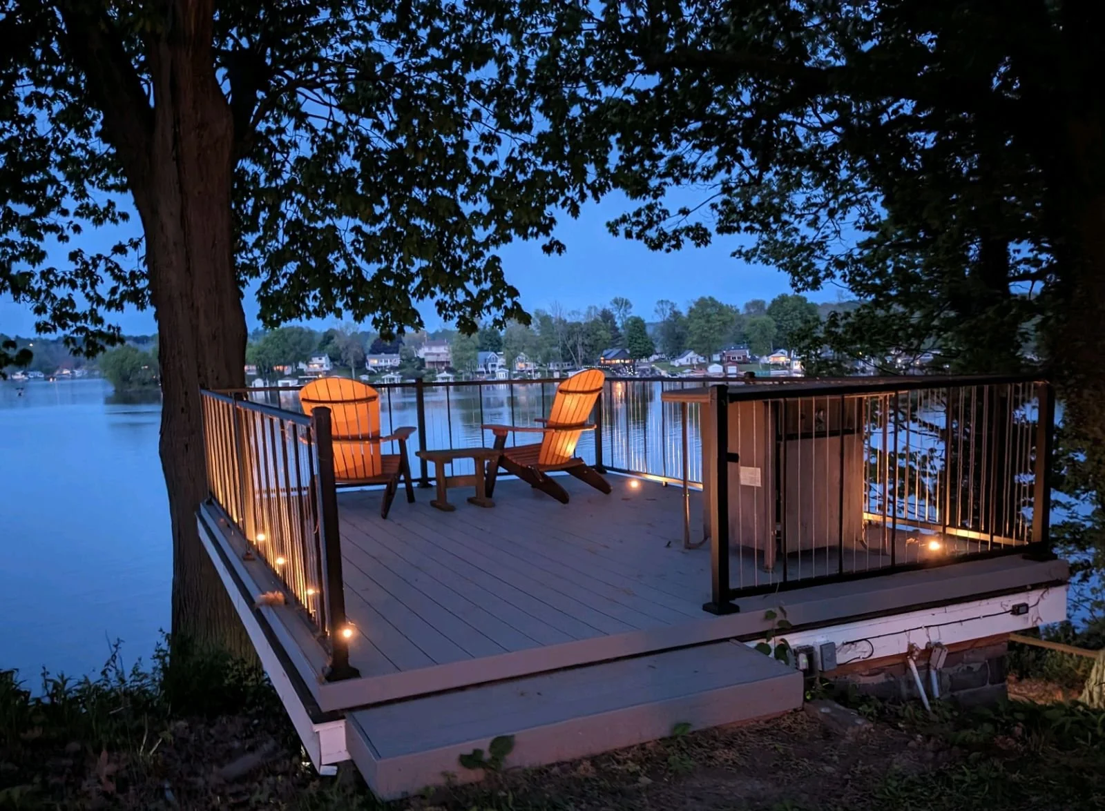 Modern deck construction at dusk, allowing to show off the functional yet decorative lighting. A simple yet sleek design to transform this lakefront back yard. 