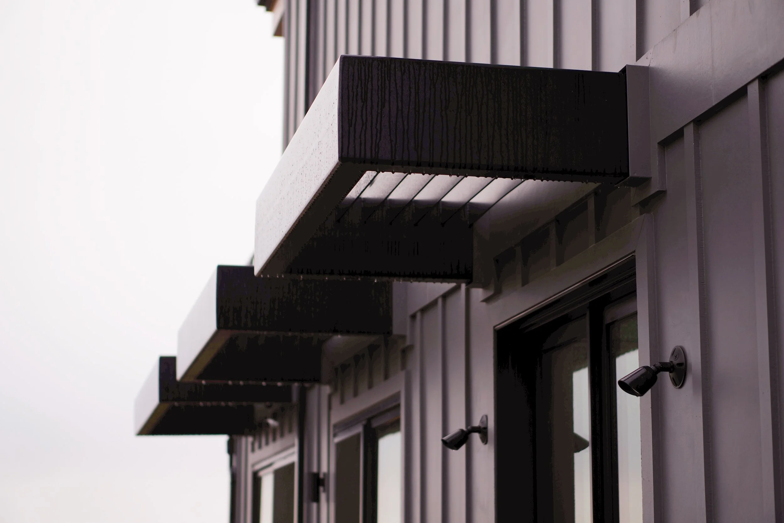 Close-up of three black rectangular balconies on a modern gray building, with outdoor spotlights mounted below each balcony.