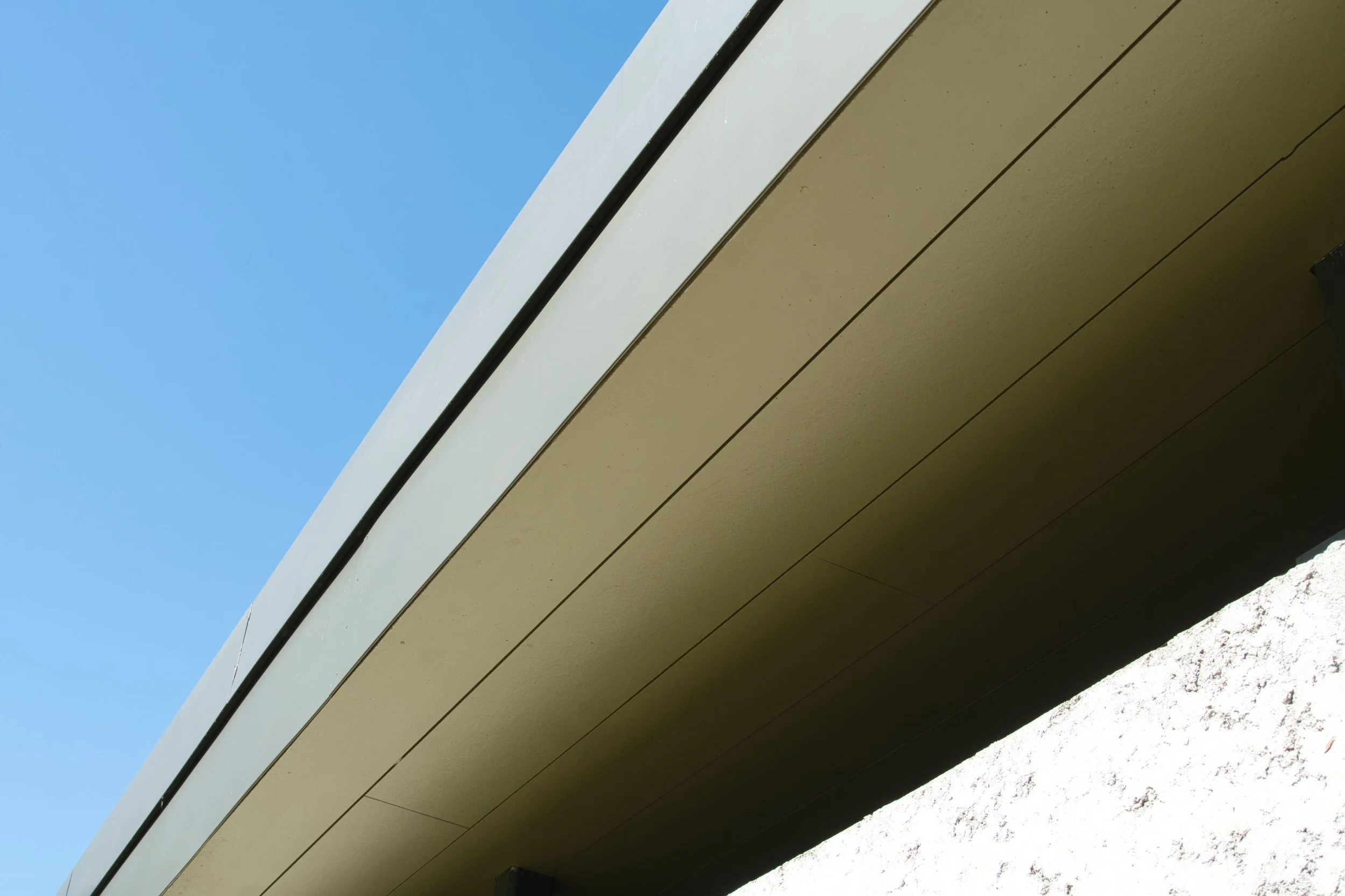 Close-up of a building's underside with beige panels, a white horizontal border, and a blue sky in the background.