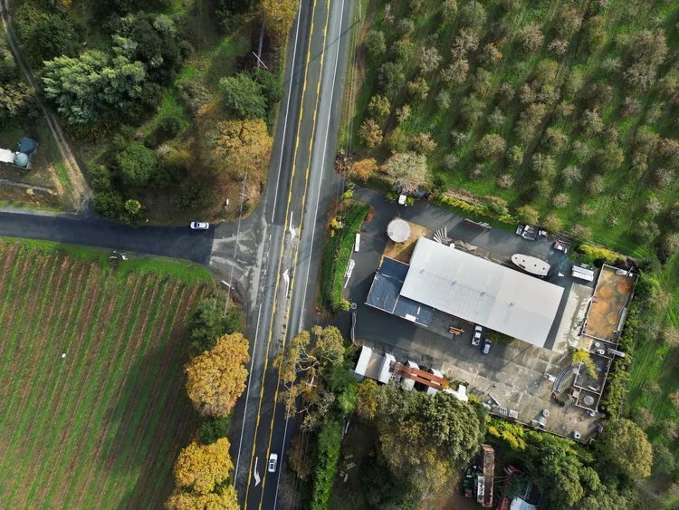 Aerial view of a rural area showing a road intersecting a farm and a residential property surrounded by trees and fields.