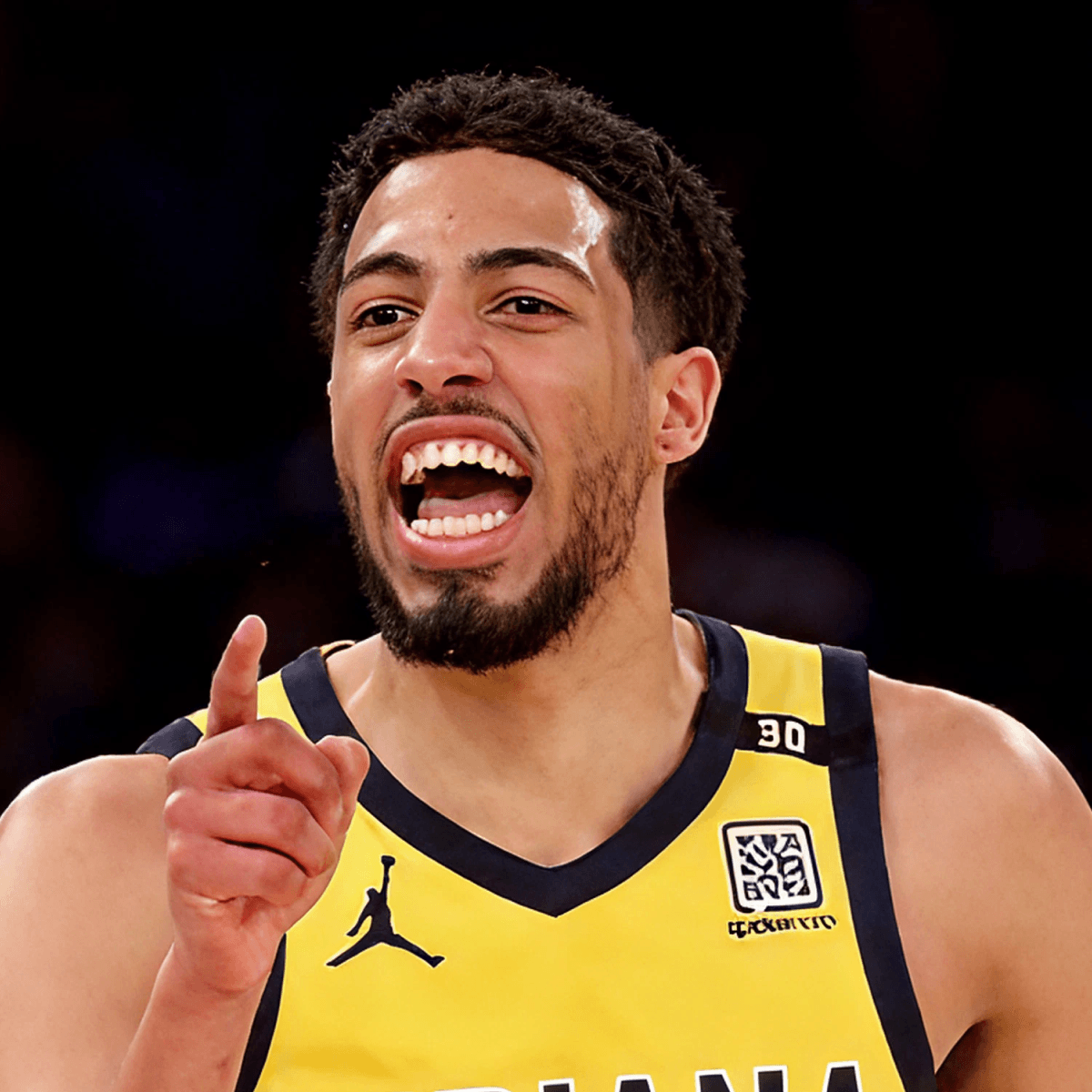 A male basketball player with a determined expression, wearing a yellow Indiana basketball jersey with navy trim and the number 0. The background shows a blurry crowd and gymnasium lights.