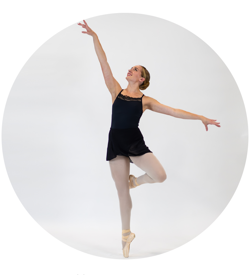 Ballet dancer in black leotard and beige tights, performing a graceful pose on pointe shoes against a white background.