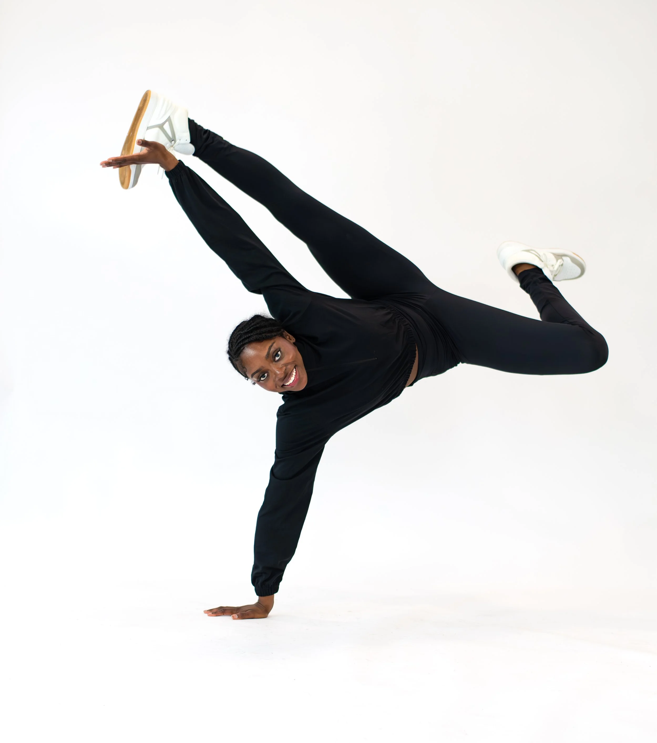 A dancer in black athletic clothing performs a handstand in a studio against a plain white background.