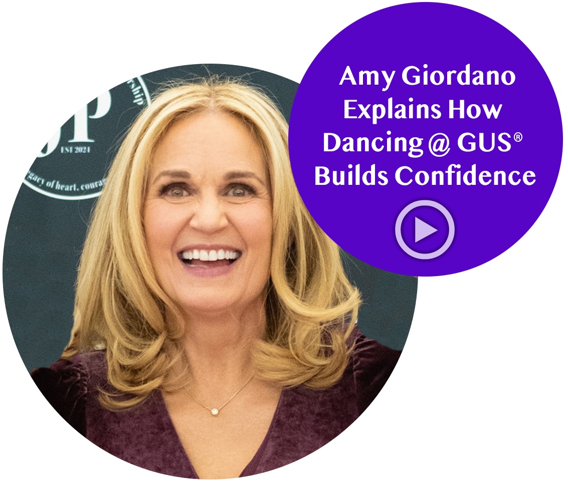 Amy Giordano with blonde hair smiling, wearing a purple top, with a purple speech bubble overlay that says "Amy Giordano Explains How Dancing @ GUS Builds Confidence" and a play button icon.