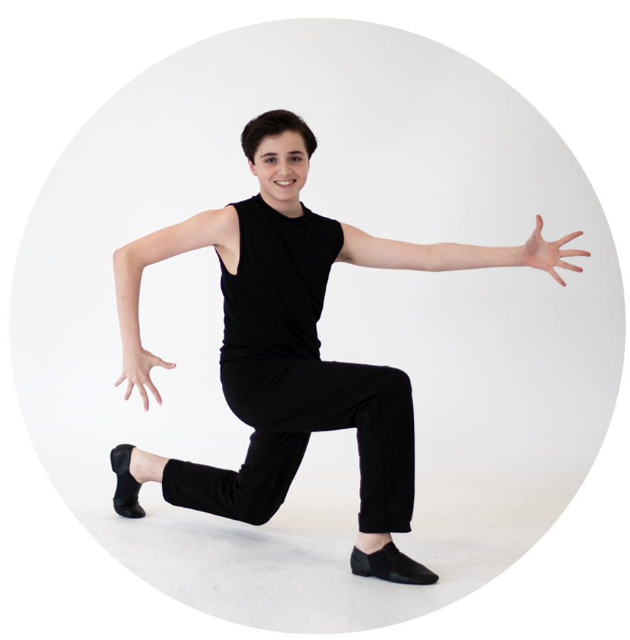 Person smiling, wearing black sleeveless shirt and black pants, crouching with one knee on the ground, extending one arm forward and the other to the side, in a dance pose or performance setting.