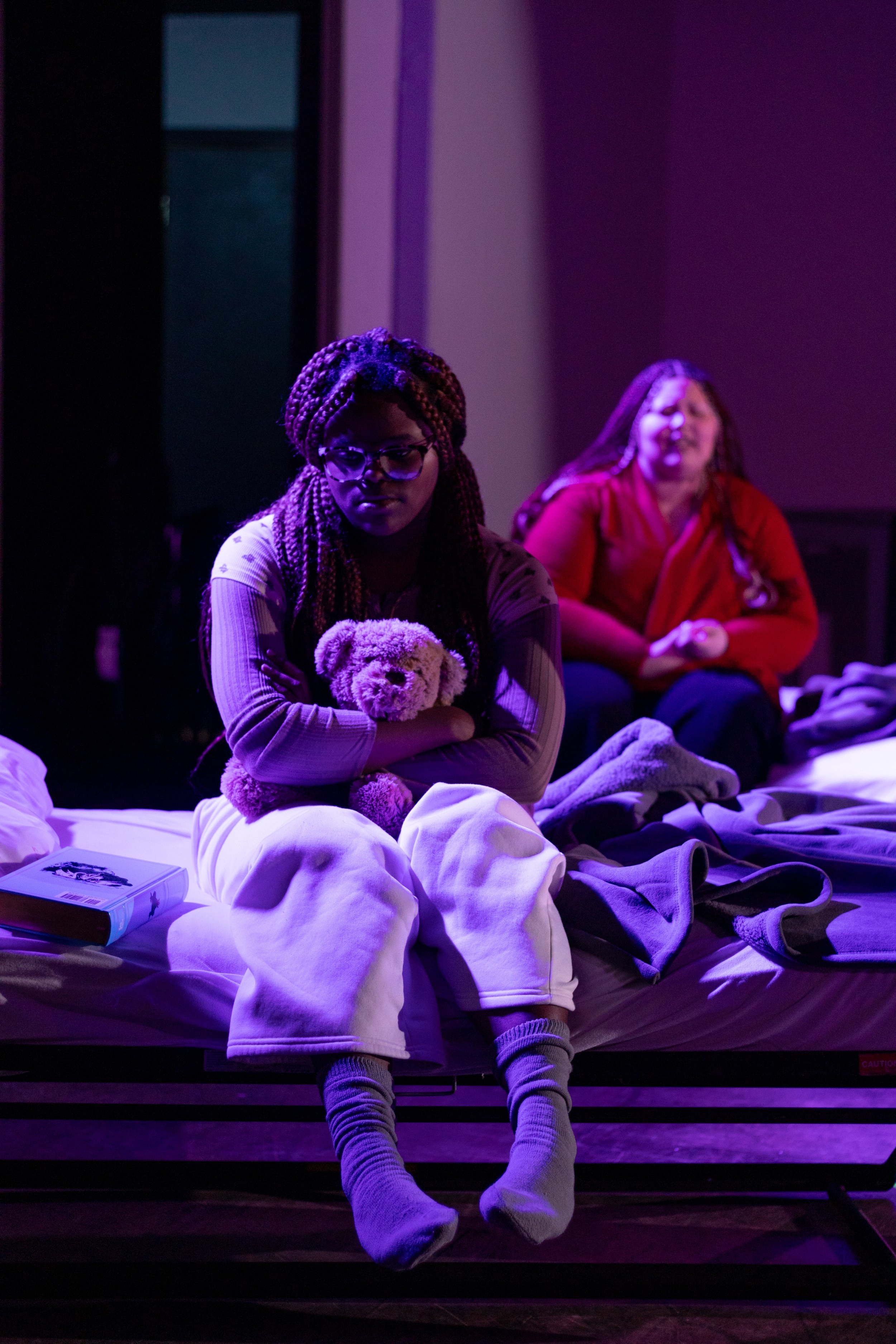 Two children in hospital gowns and pajamas sitting in blue chairs, one holding a teddy bear.