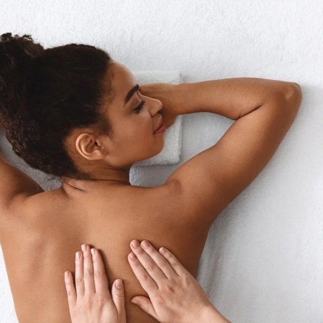 A woman with curly hair lying on her side with her eyes closed, receiving a back massage.