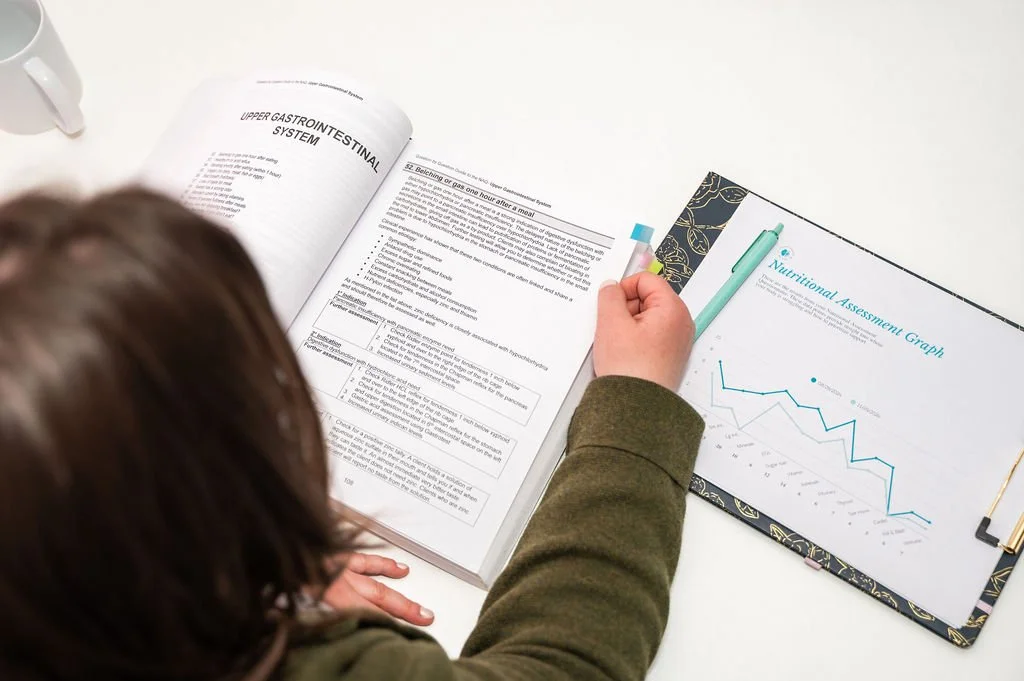 Person reviewing medical textbooks and nutritional assessment graph on a white desk.