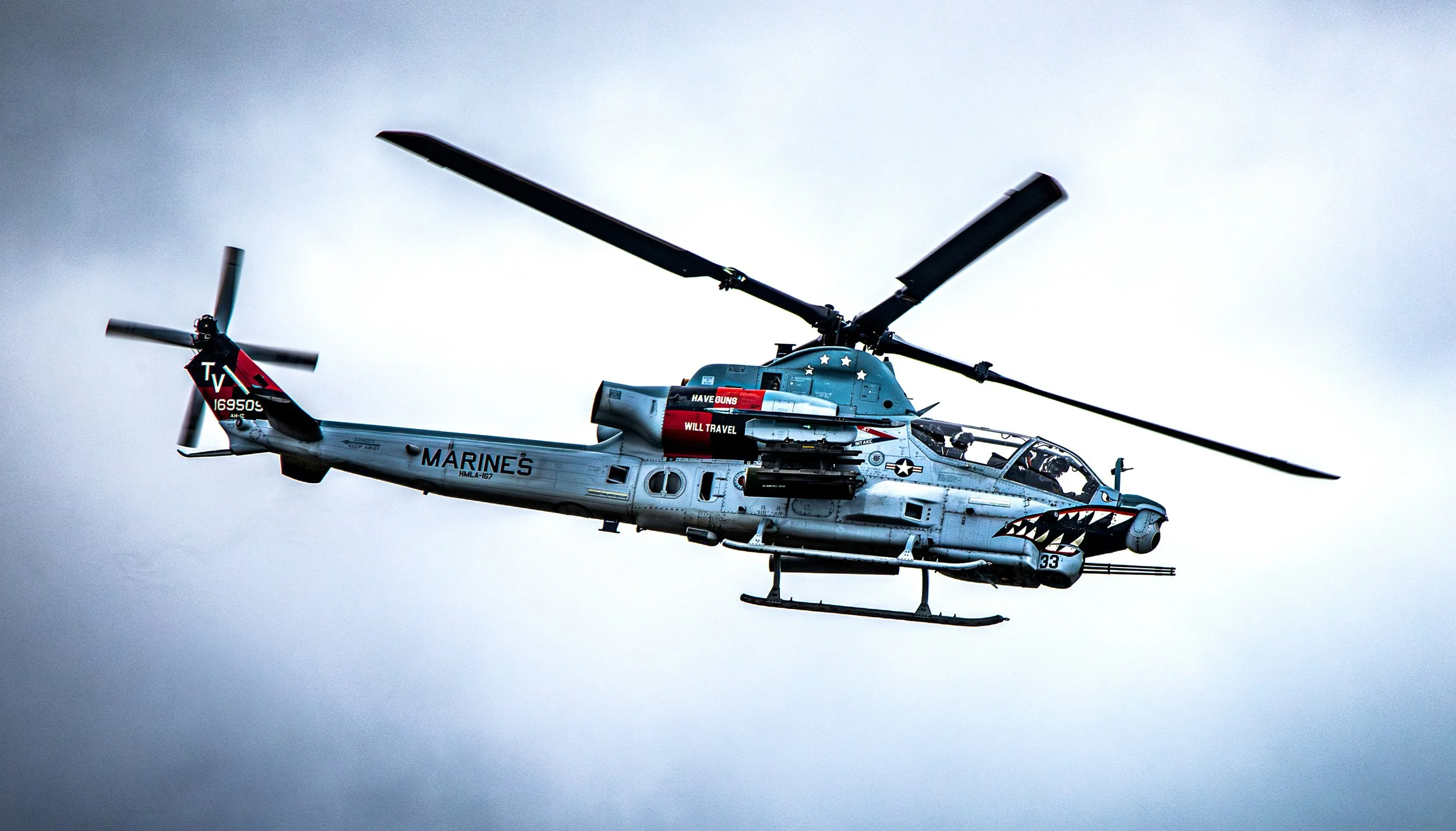 A military helicopter flying in the sky, painted with shark face design on the front, with various markings and text on its body.