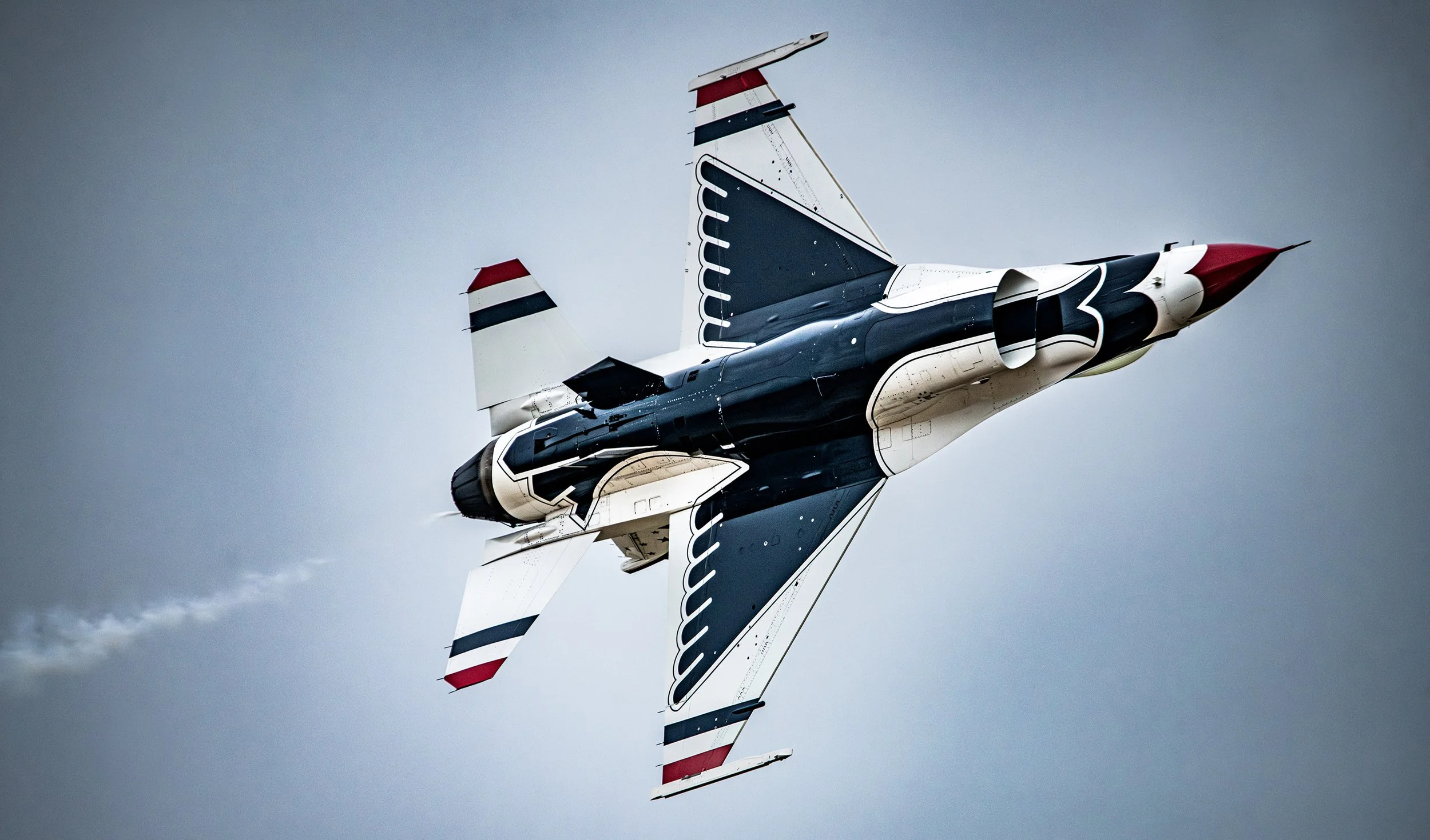 A fighter jet soaring through the sky with a sleek black and white design accented with red, blue, and white stripes on its tail fins, and emitting smoke from its engine.