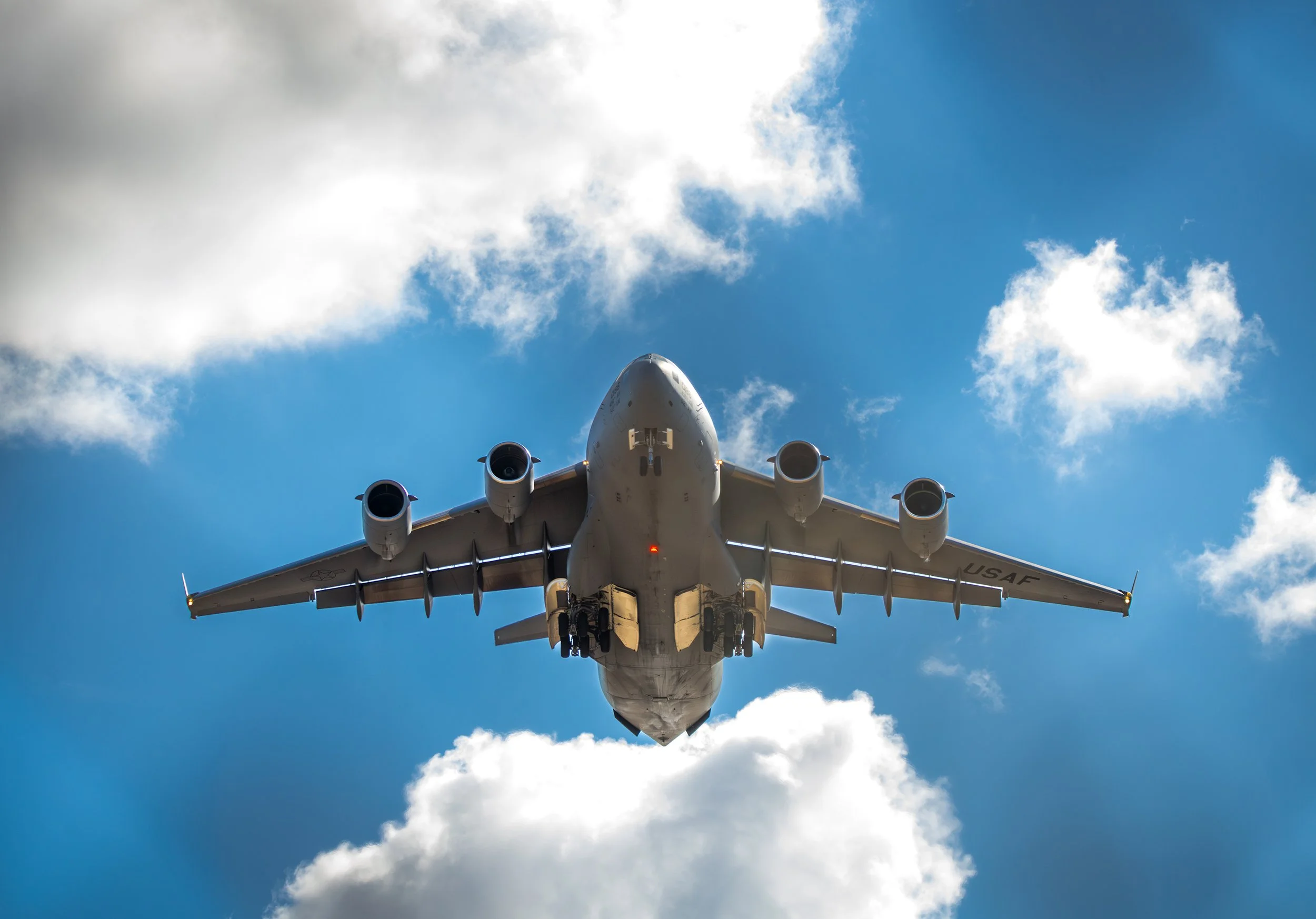 A large military cargo airplane flying in the sky with blue sky and clouds in the background.