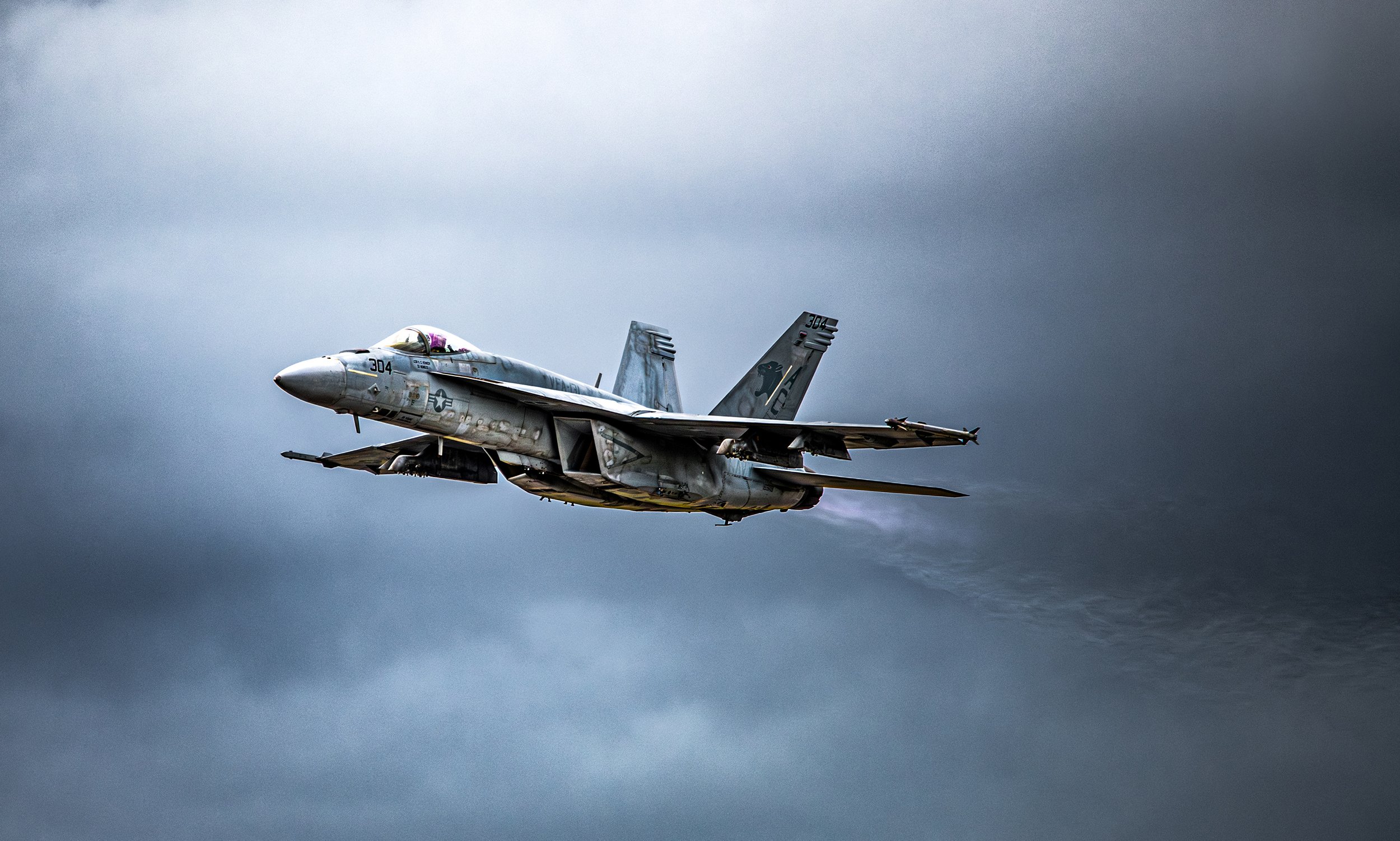 A military fighter jet flying against a cloudy sky.