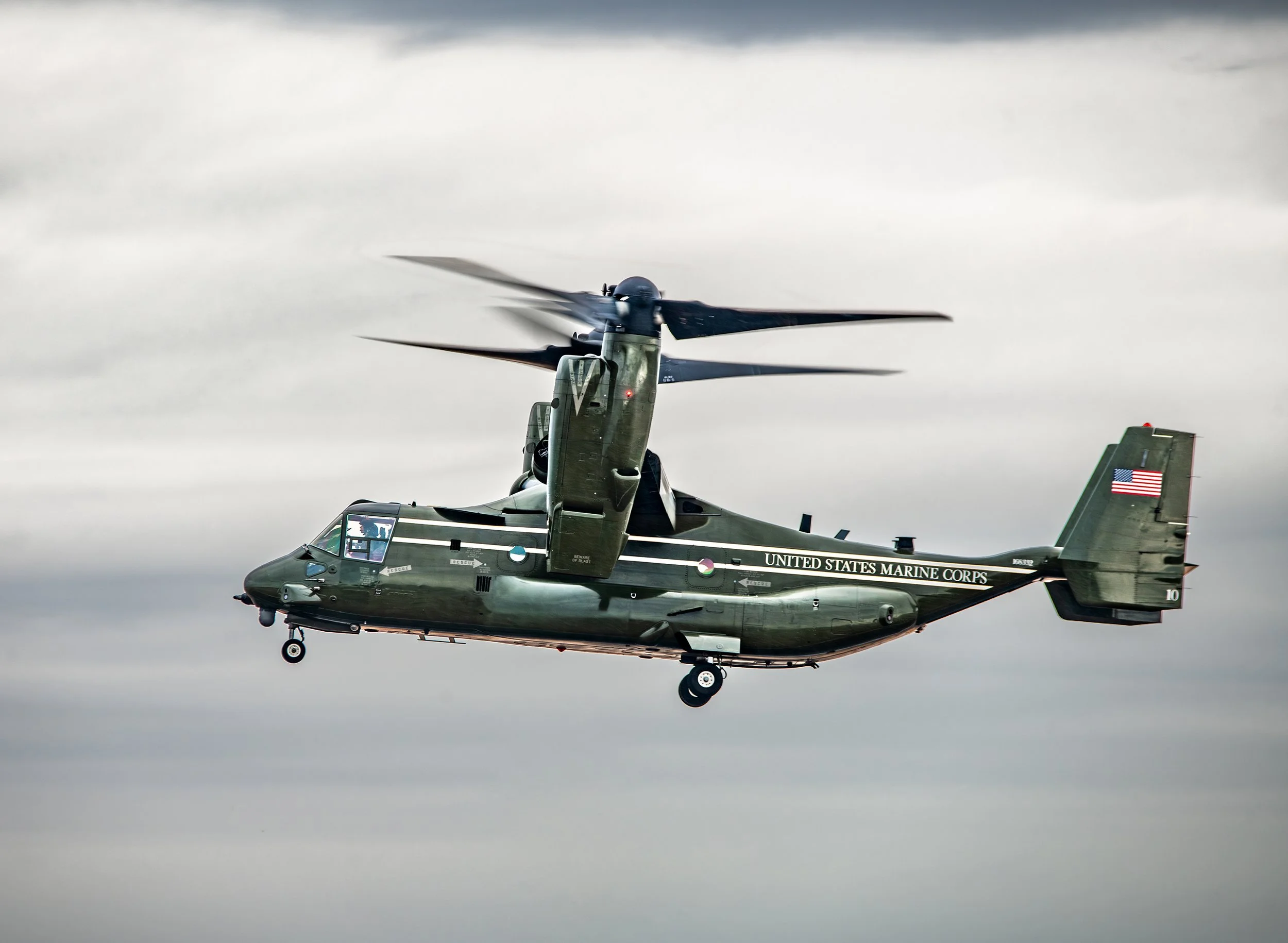 A green United States Marine Corps helicopter in flight against a cloudy sky.