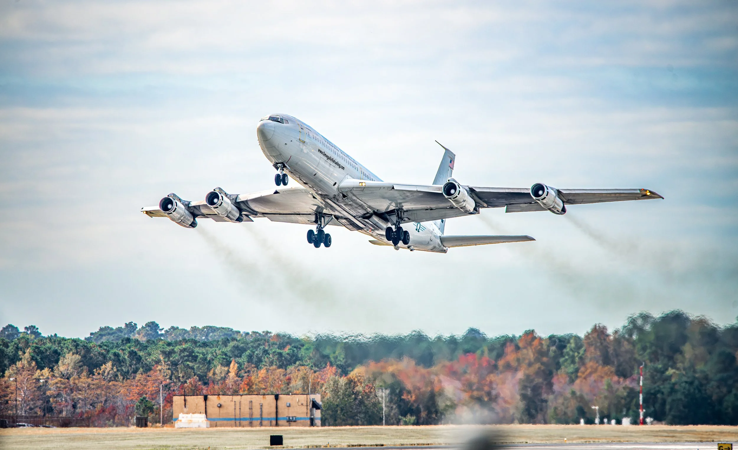 A commercial airplane taking off from the runway, ascending into the sky with trees and buildings in the background.