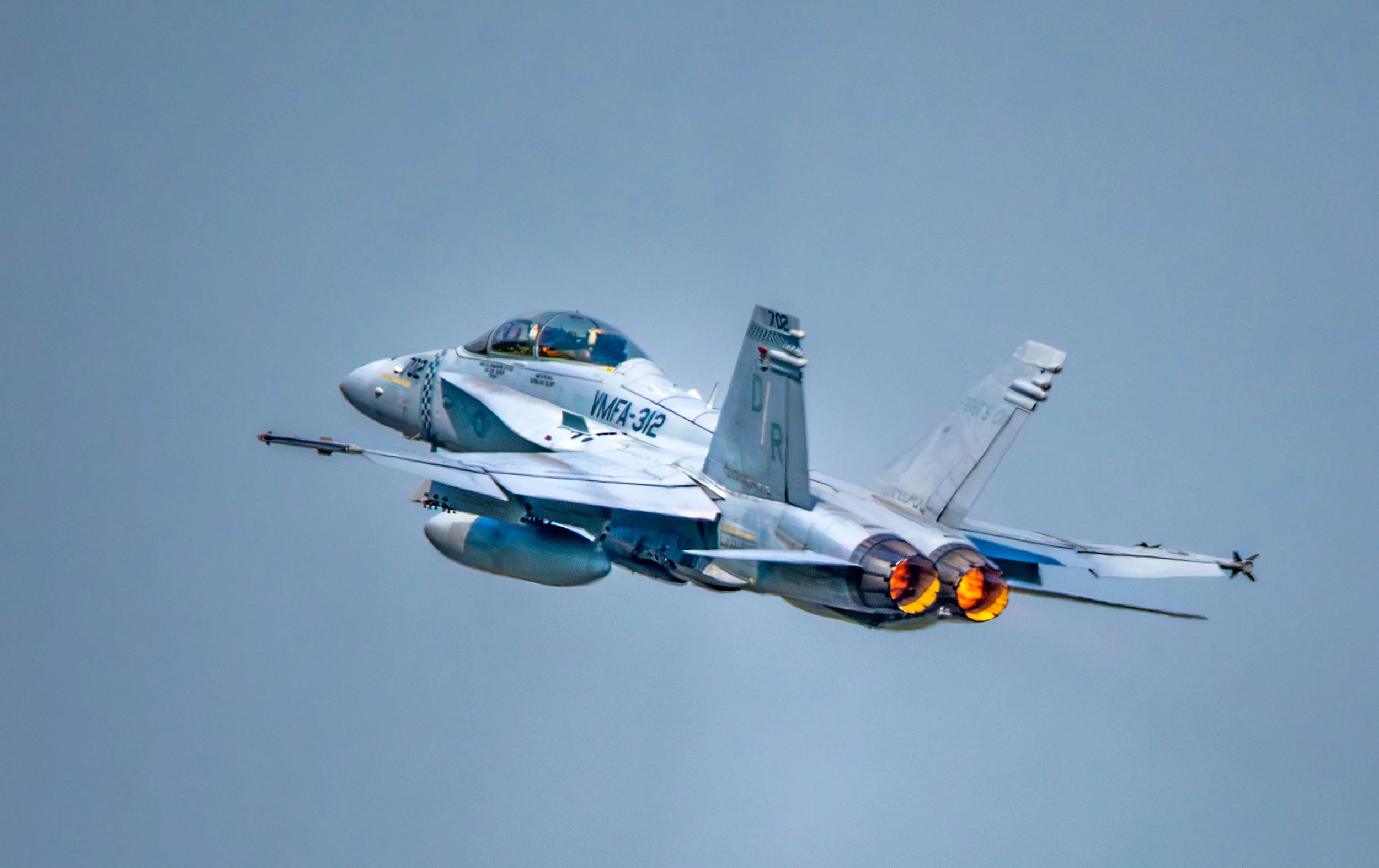 F-22 fighter jet flying with afterburners on against a clear sky.
