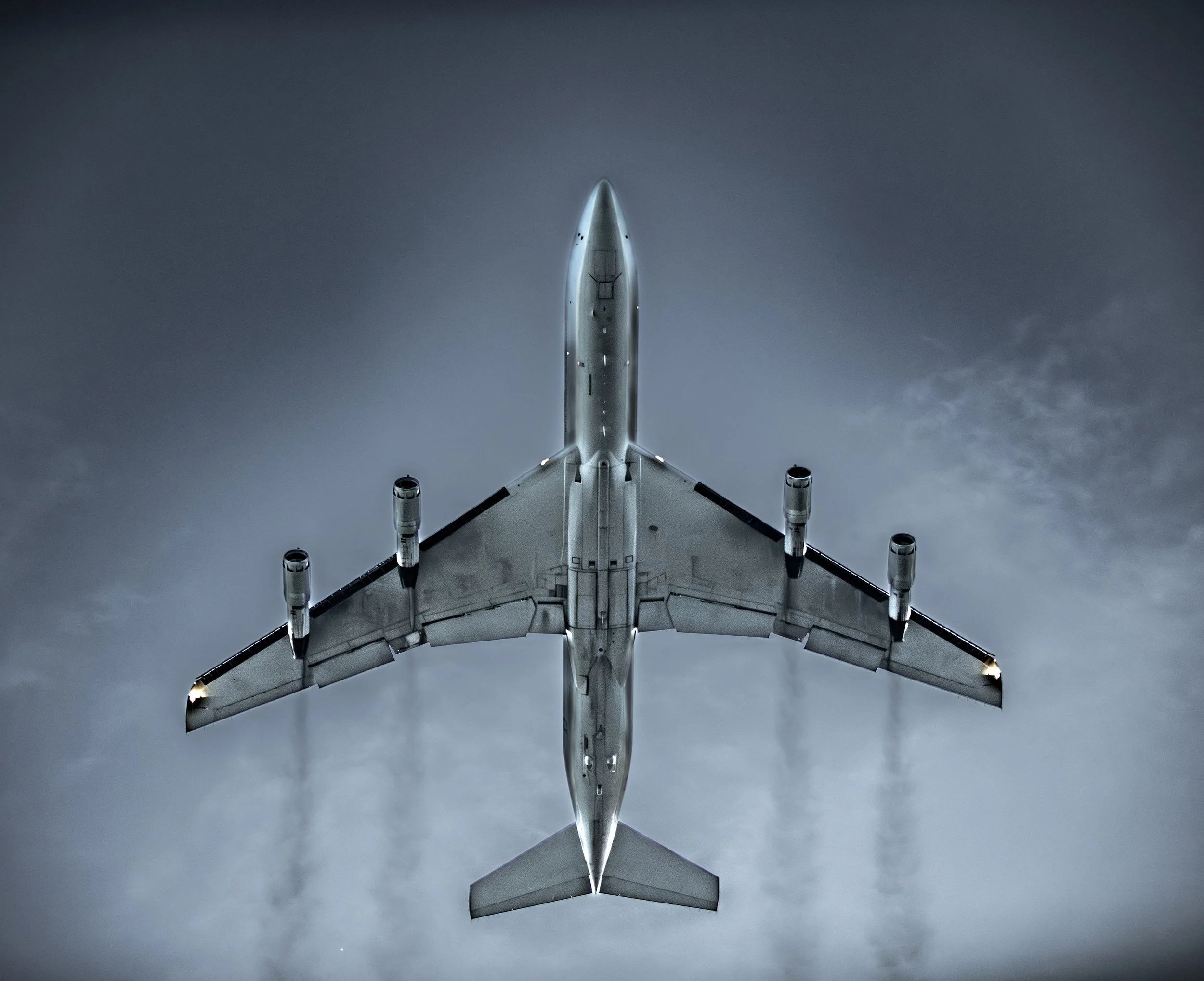 A large commercial airplane flying overhead seen from below against a cloudy sky.