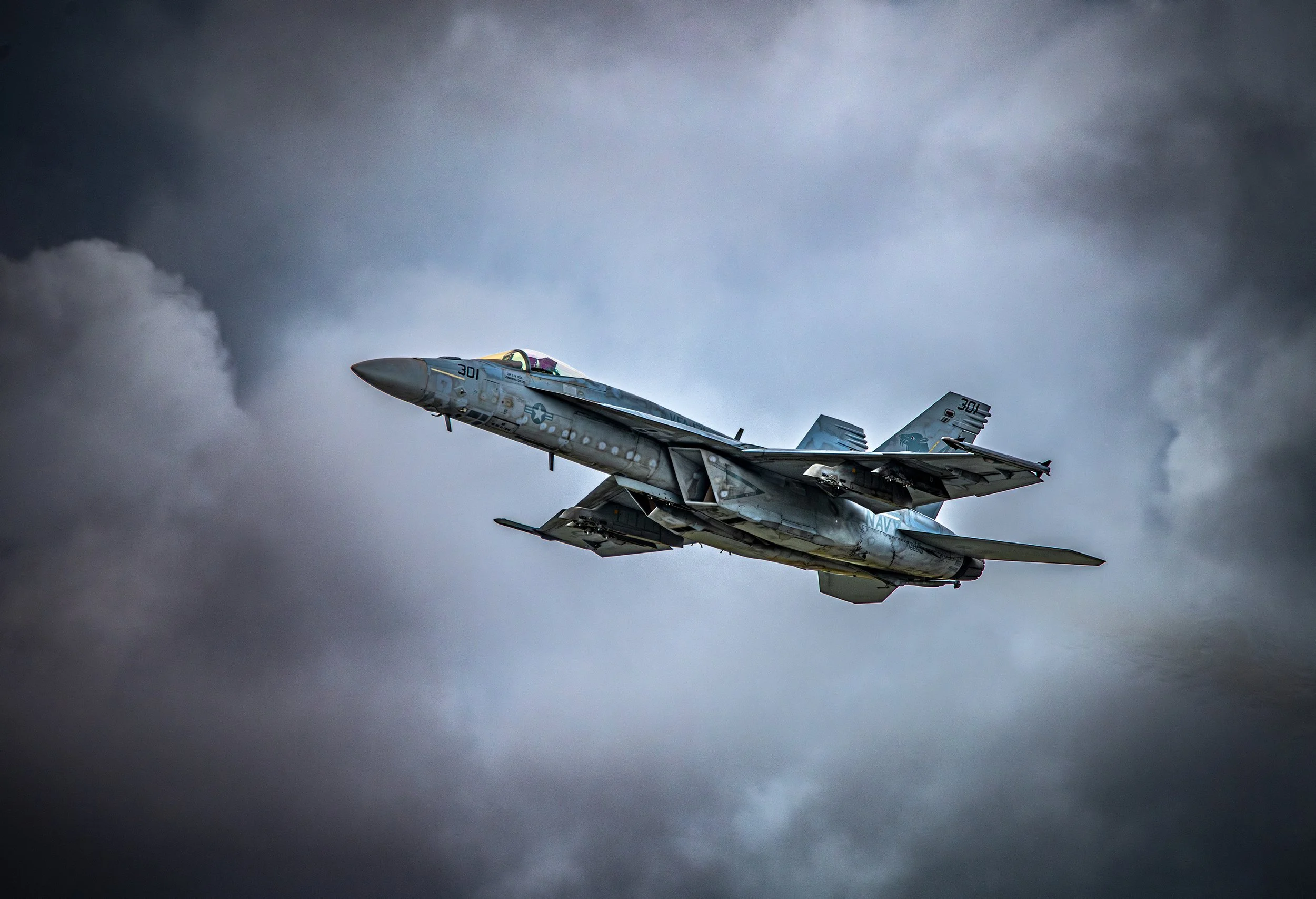 A military jet flying through dark, cloudy skies.