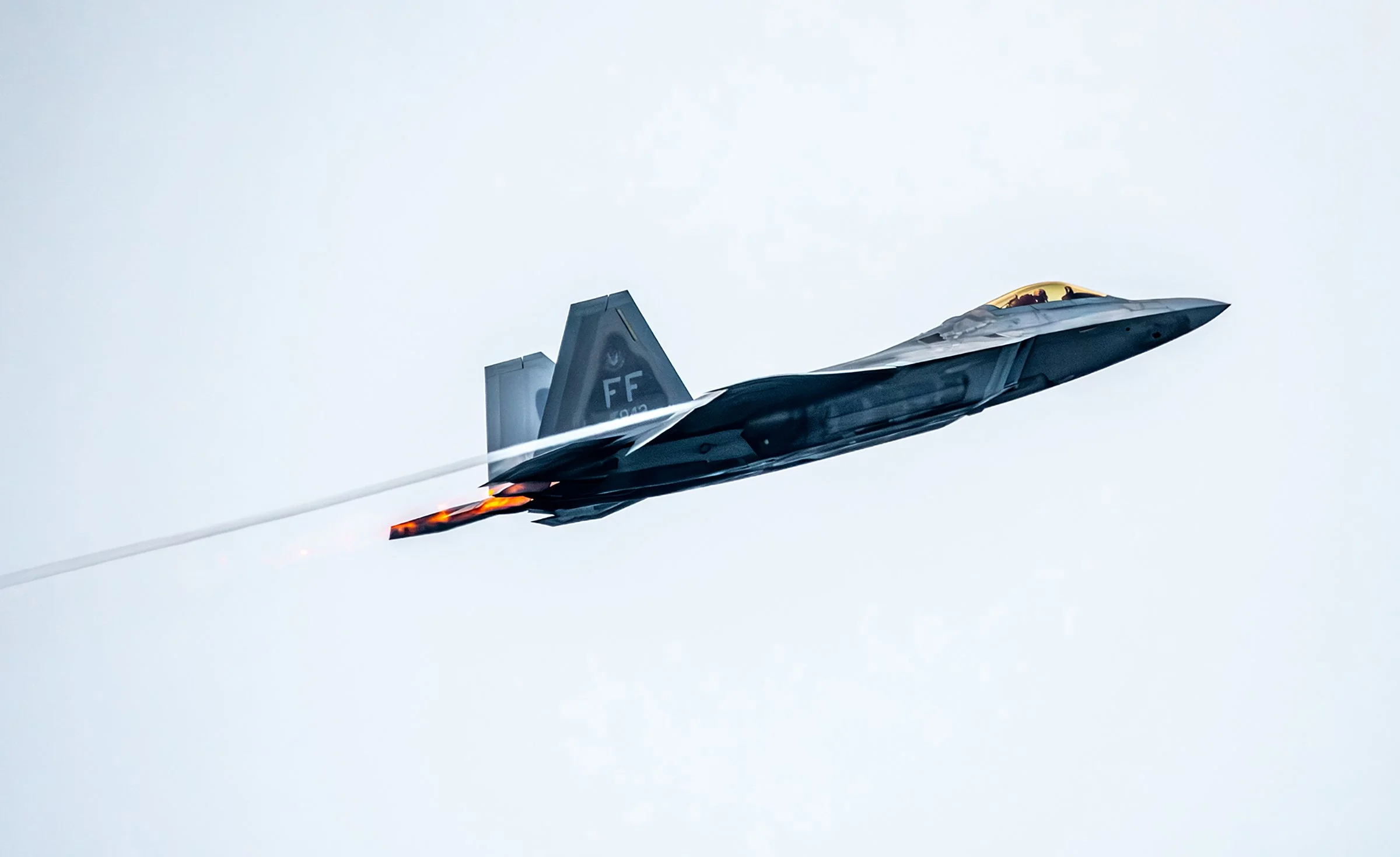 A fighter jet flying in the sky with afterburners engaged, emitting flames and vapor trails.