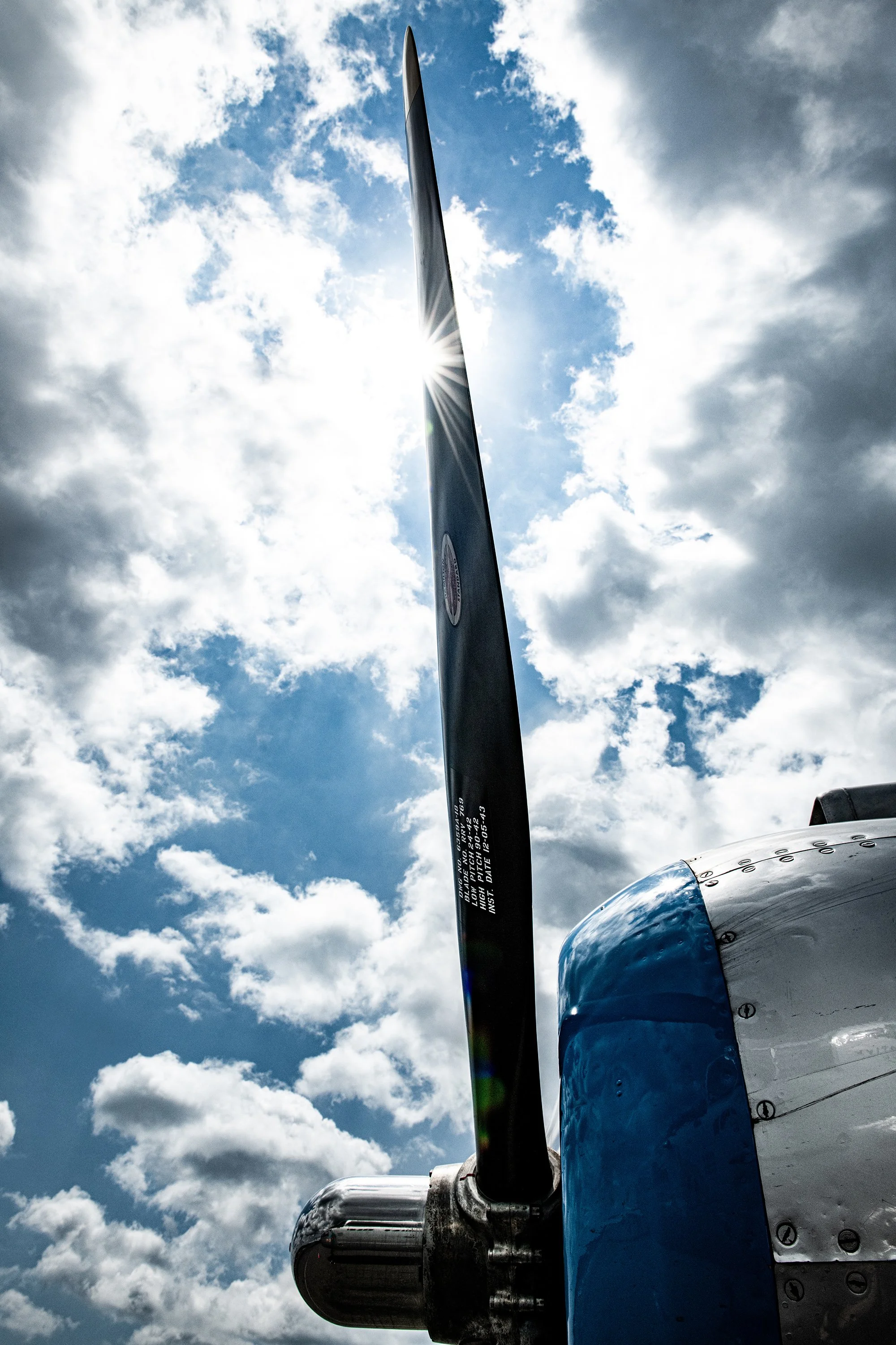 Close-up of an aircraft propeller with a bright sun behind, sky with clouds in the background.