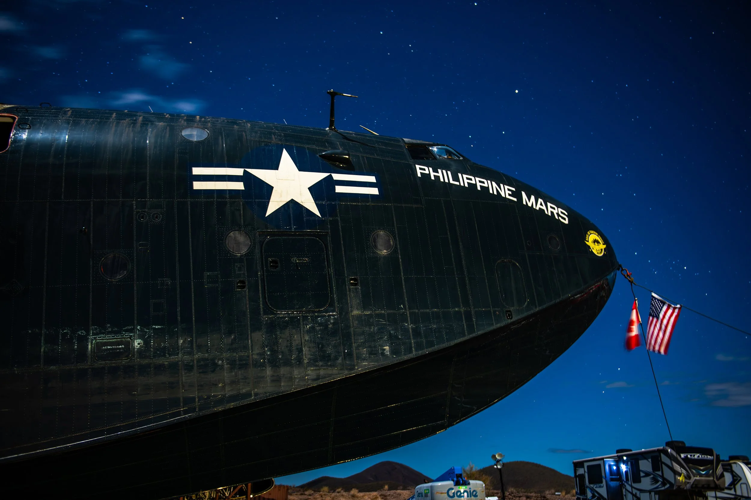 A black military helicopter with the words 'Philippine Mars' and a white star insignia, flying at night under a starry sky, with American flags attached to its nose.
