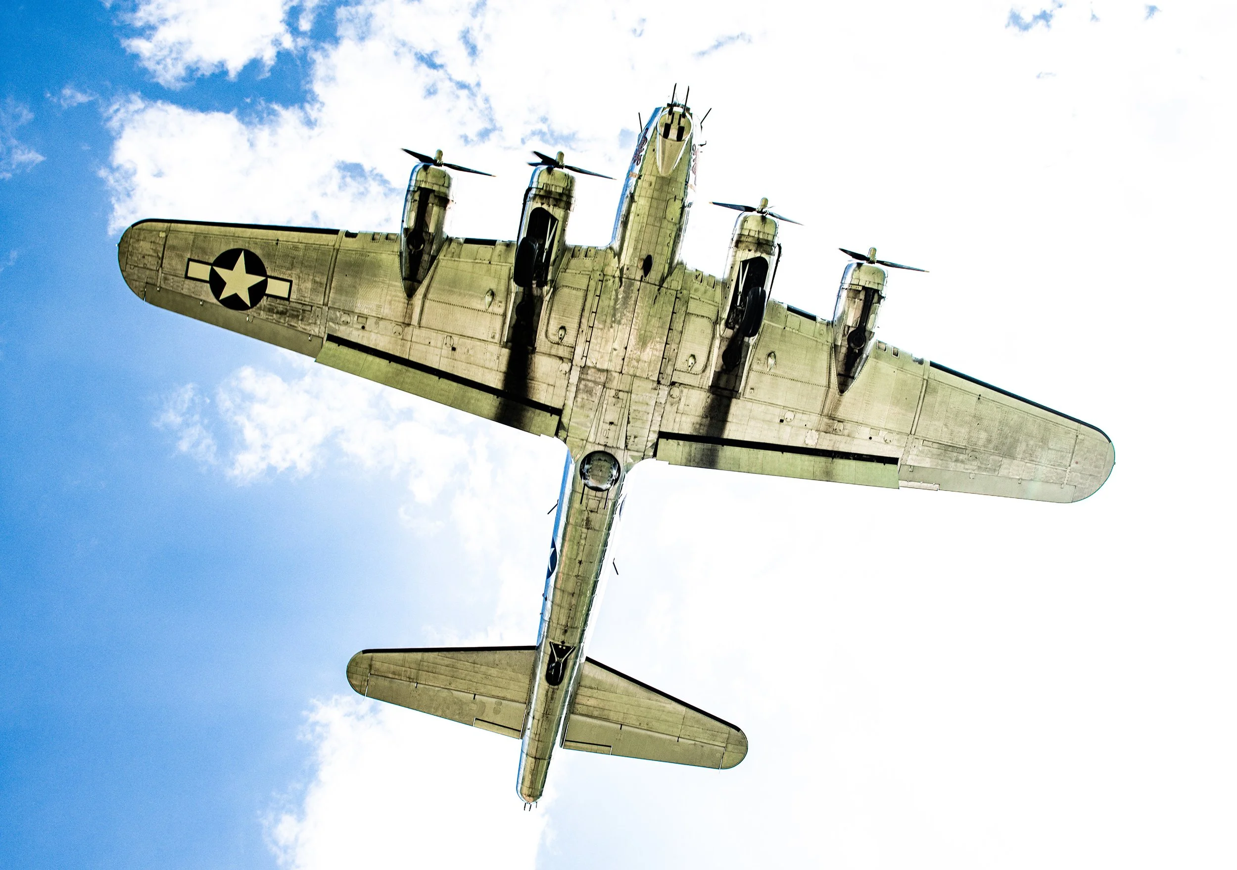 A military aircraft flying overhead against a partly cloudy sky, viewed from below.