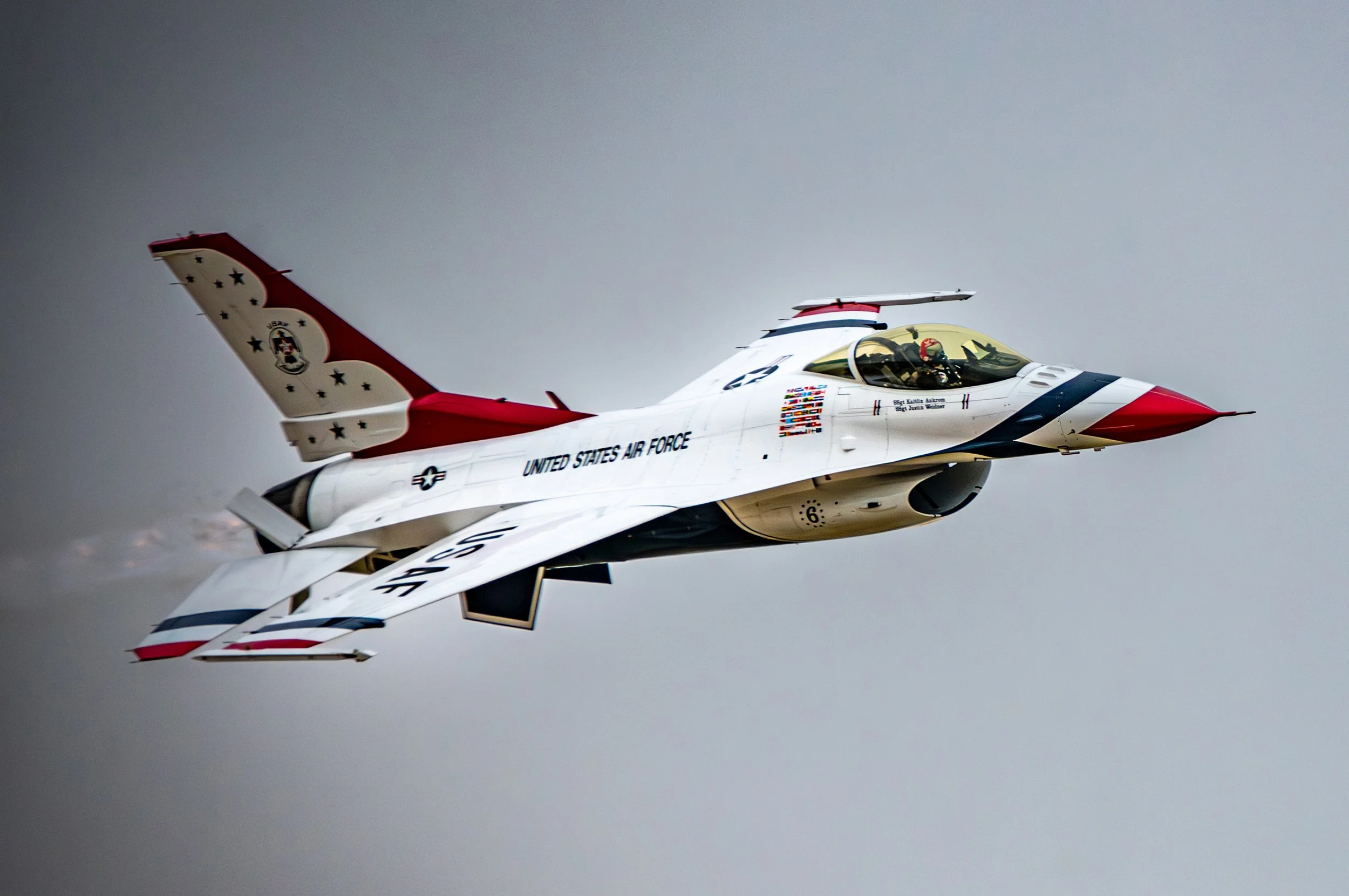 F-16 fighter jet with U.S. Air Force markings and red, white, and blue patriotic paint scheme flying in overcast sky.