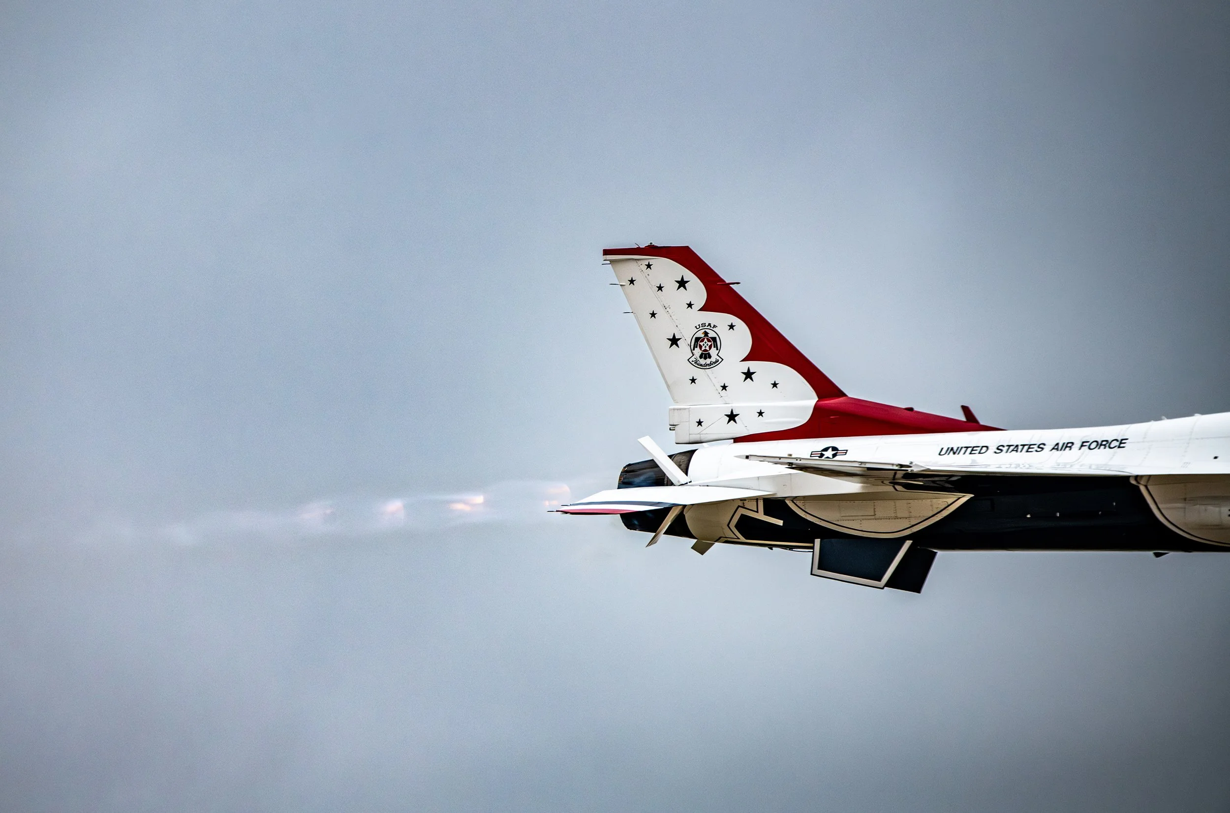 A United States Air Force aircraft flying in the sky, with visible jet exhaust and a decorated tail fin featuring stars and a logo.