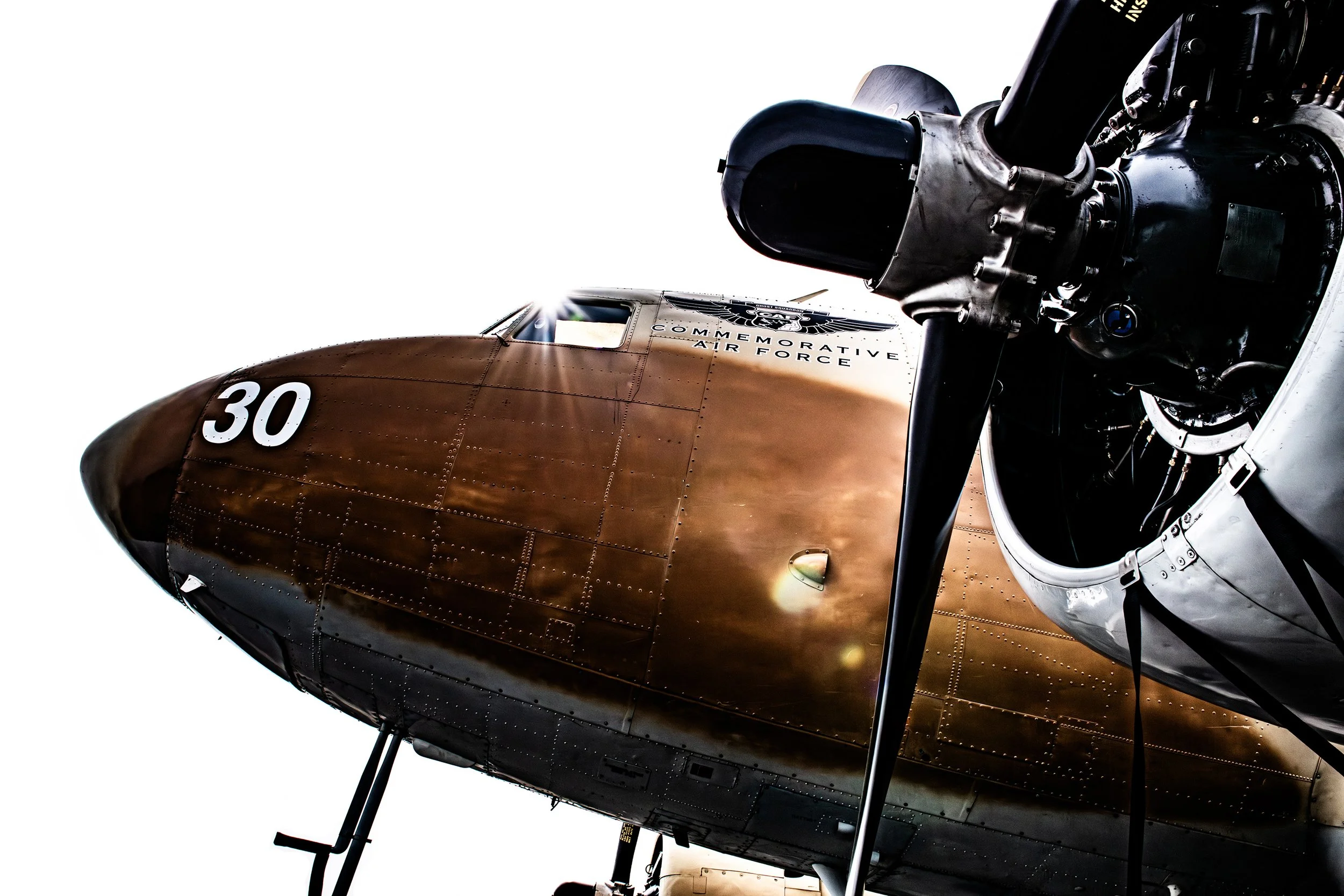 A vintage military aircraft with a bronze-colored nose, black propeller, and white number 30 on the fuselage, commemorating the Air Force, viewed from below against a bright sky.