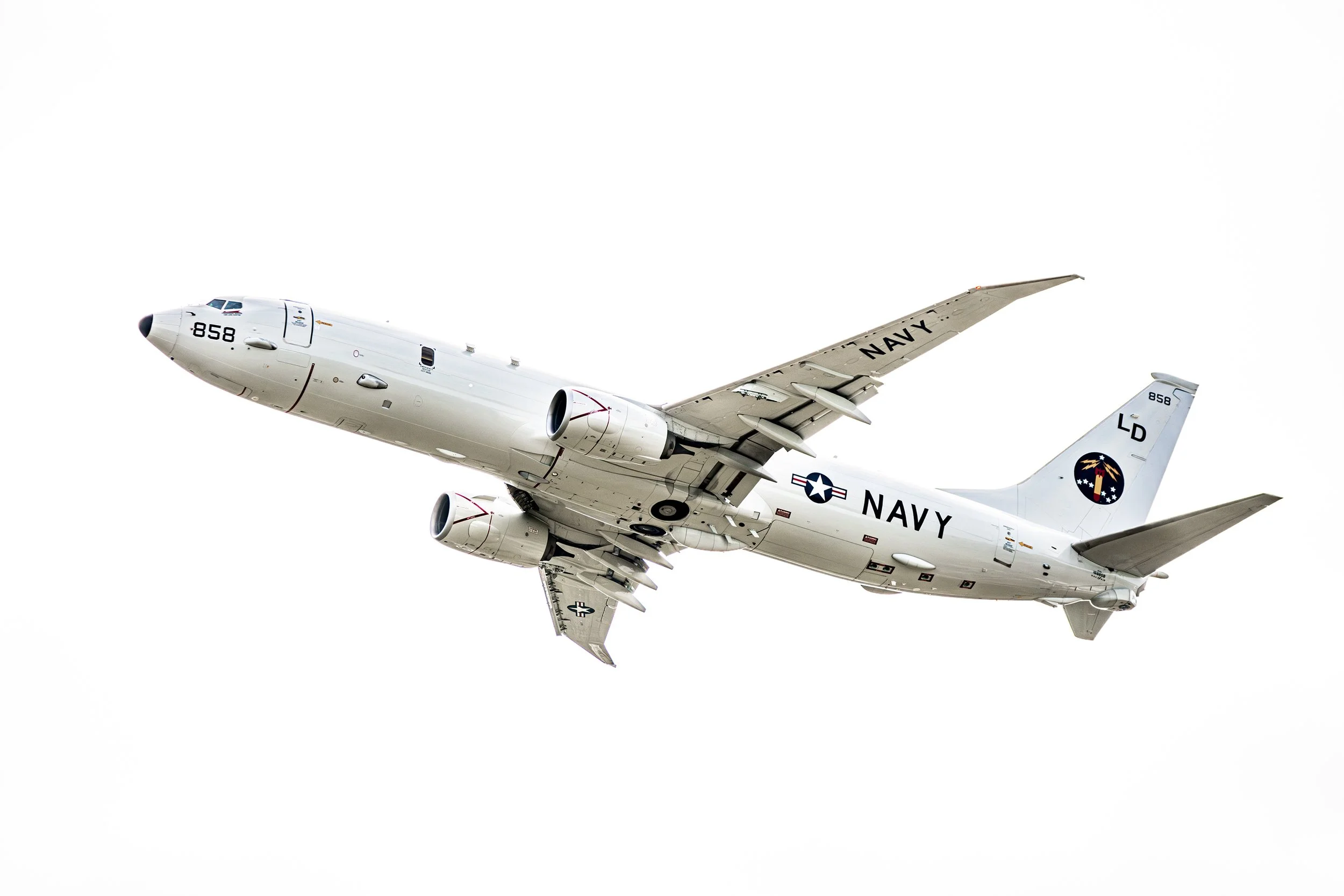 A white Navy aircraft flying in the sky with visible Navy markings and insignia.