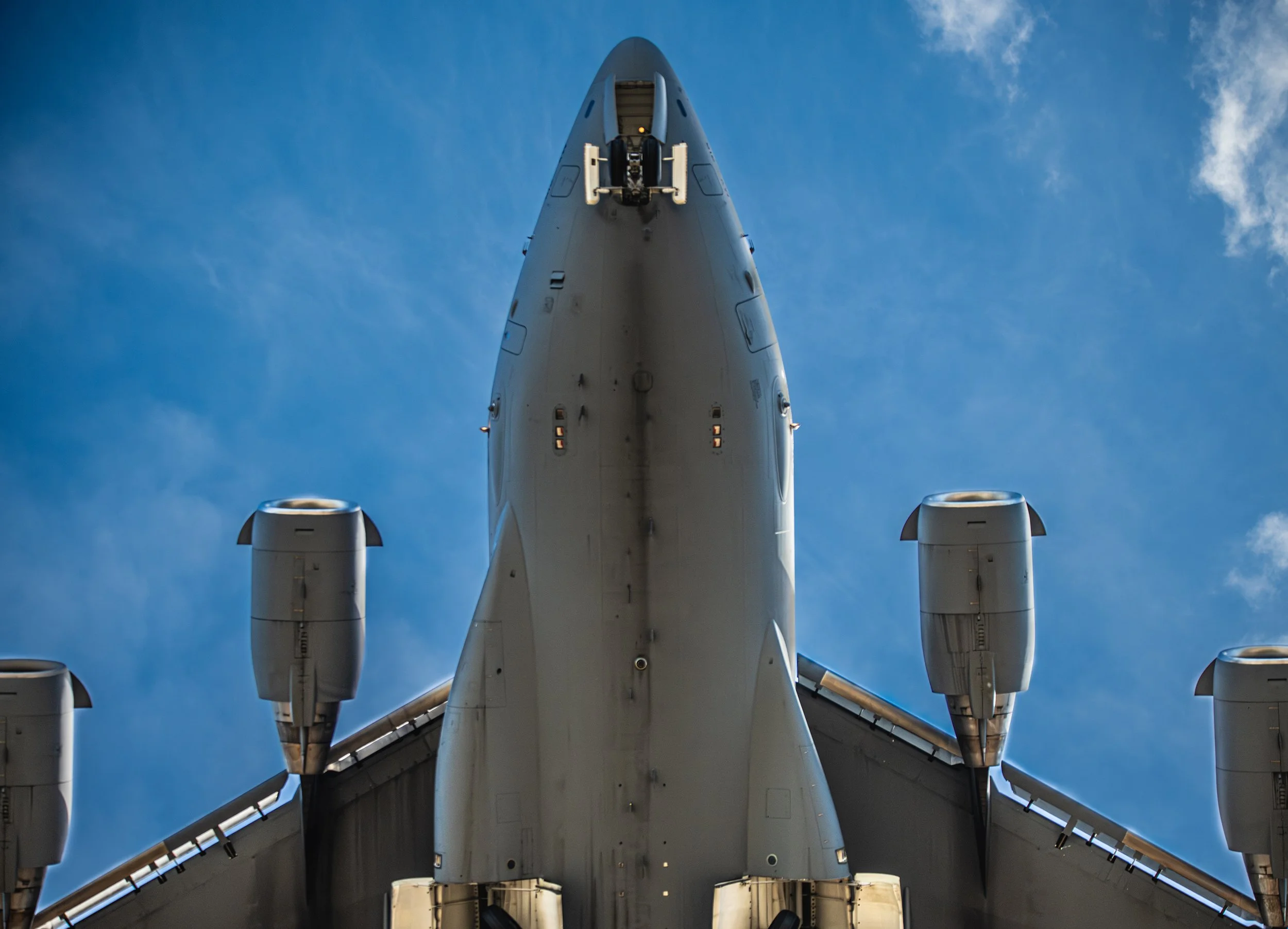 Close-up view of the underside of a large commercial airplane in flight, showing its four engines and wings against a blue sky.