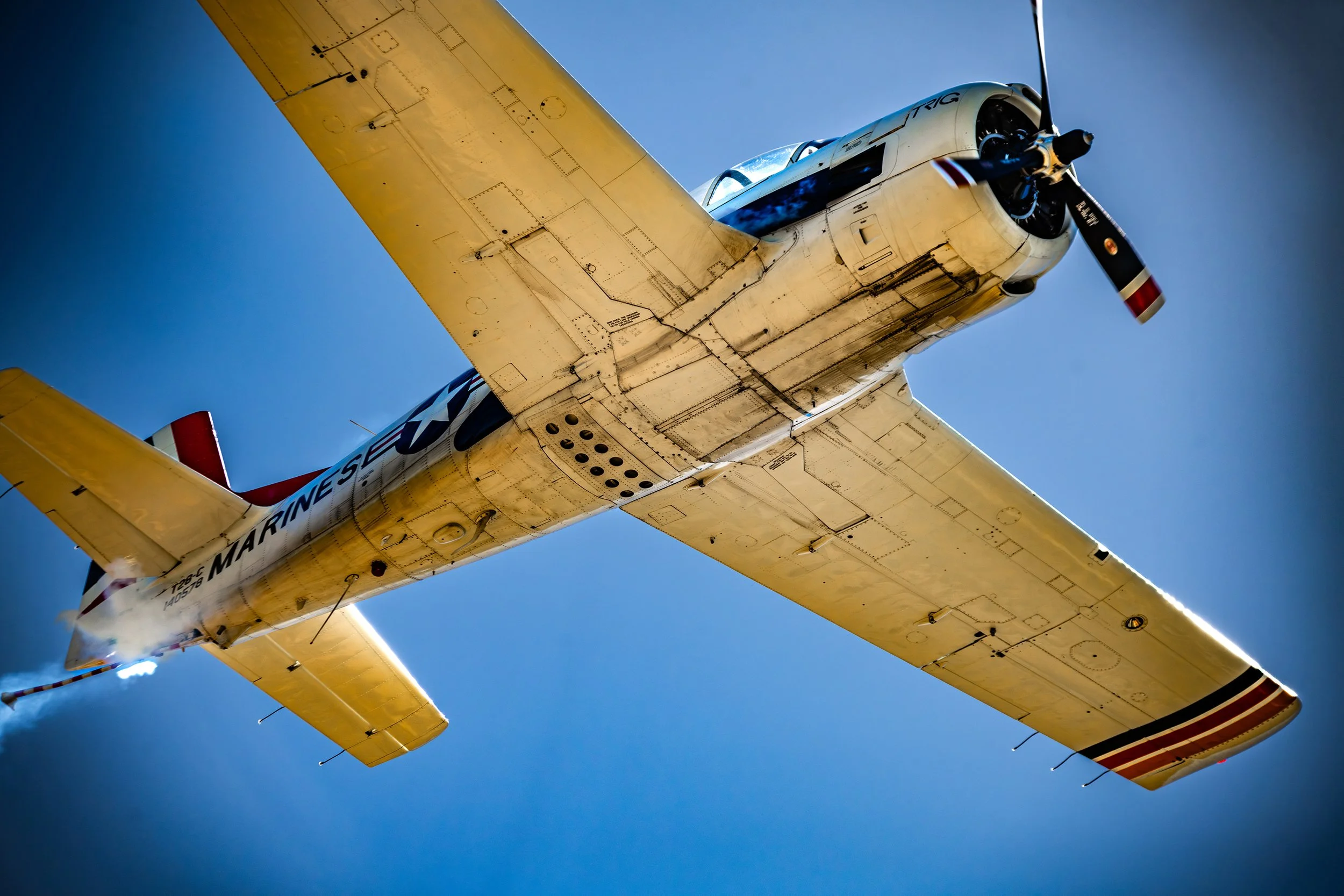 A military aircraft flying in the sky, viewed from below, with the word 'MARINES' visible on the side.