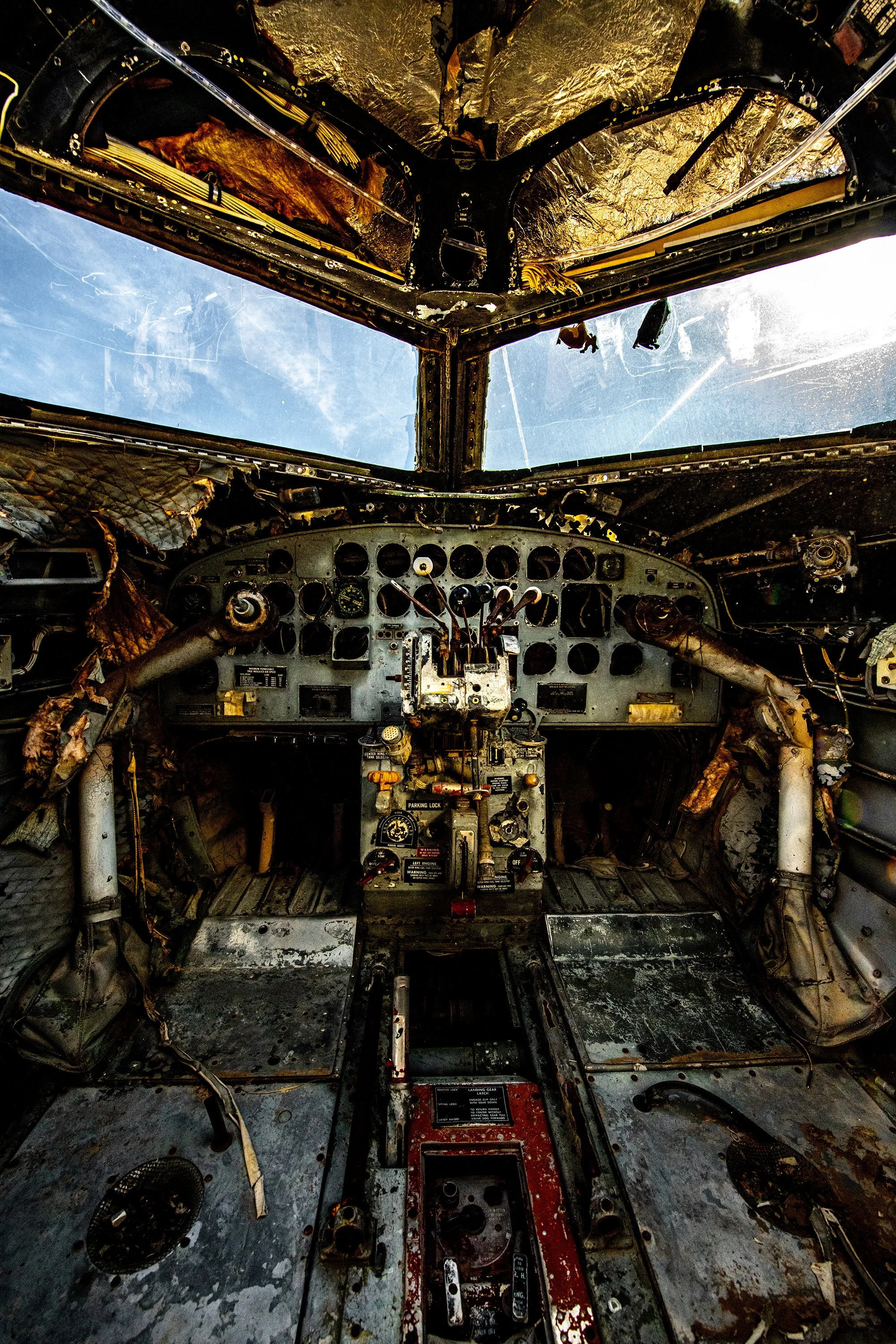 Interior of an abandoned aircraft cockpit with damaged controls, exposed wiring, and deteriorated surfaces.