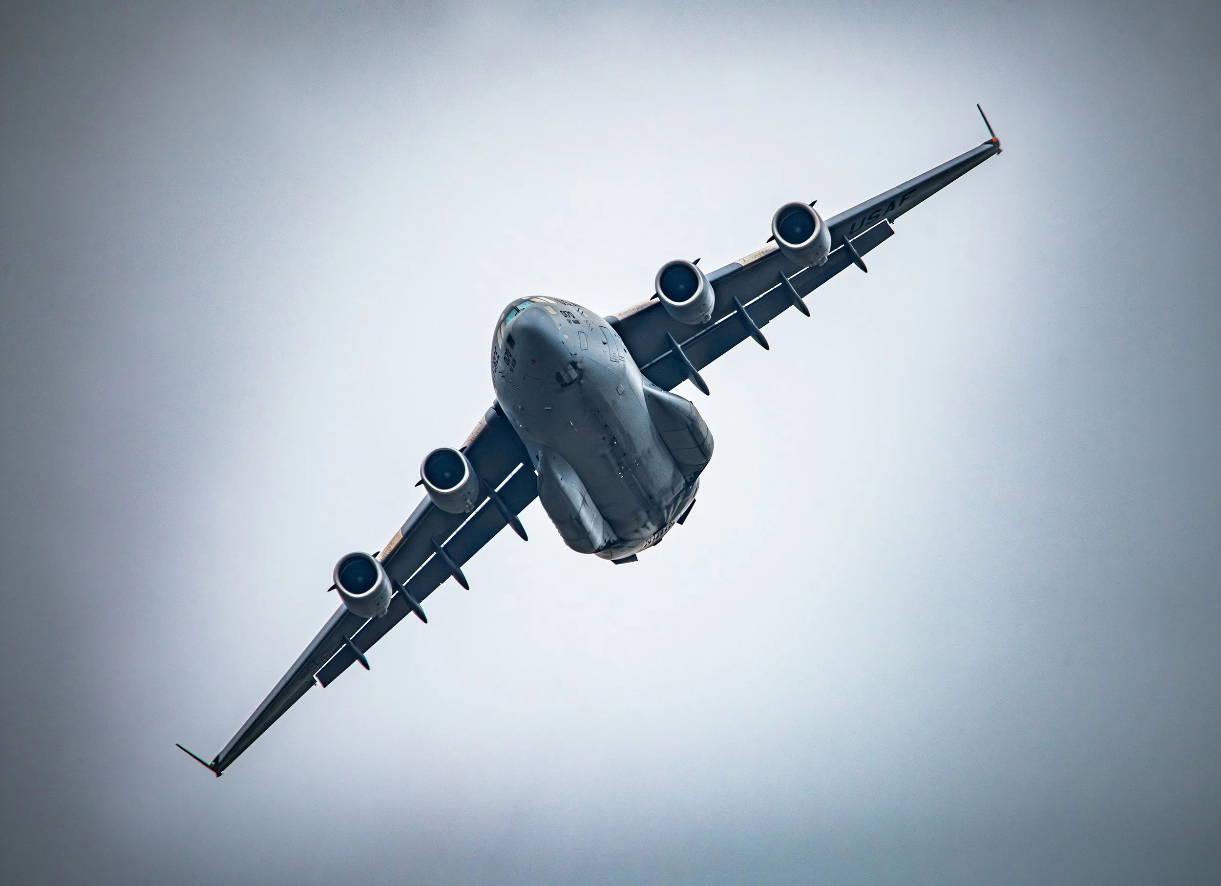 A military cargo plane flying in the sky with a mostly gray background.